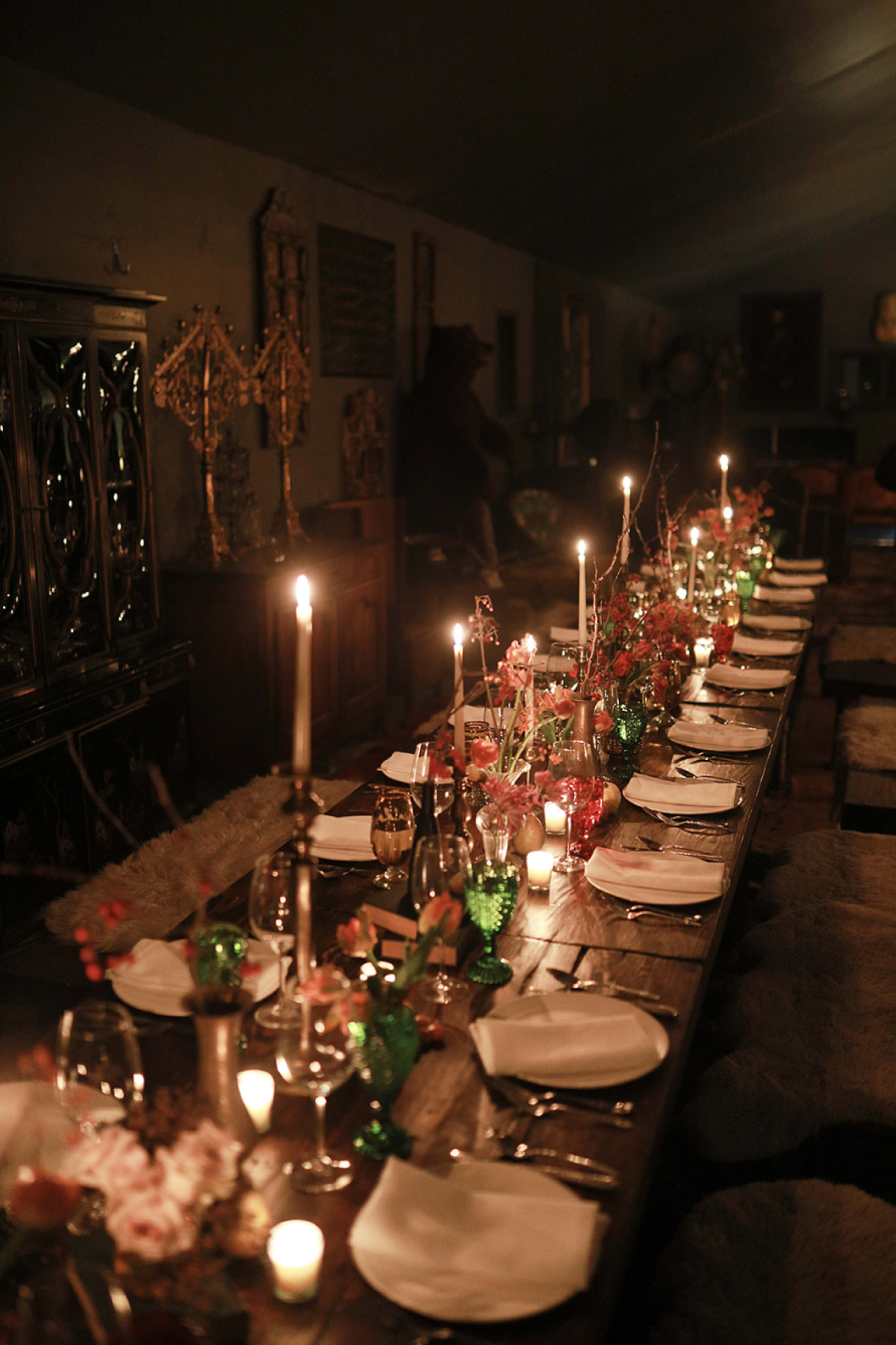 A long, wooden dining table is set with plates, candles, and decorative flowers in a dimly lit room.