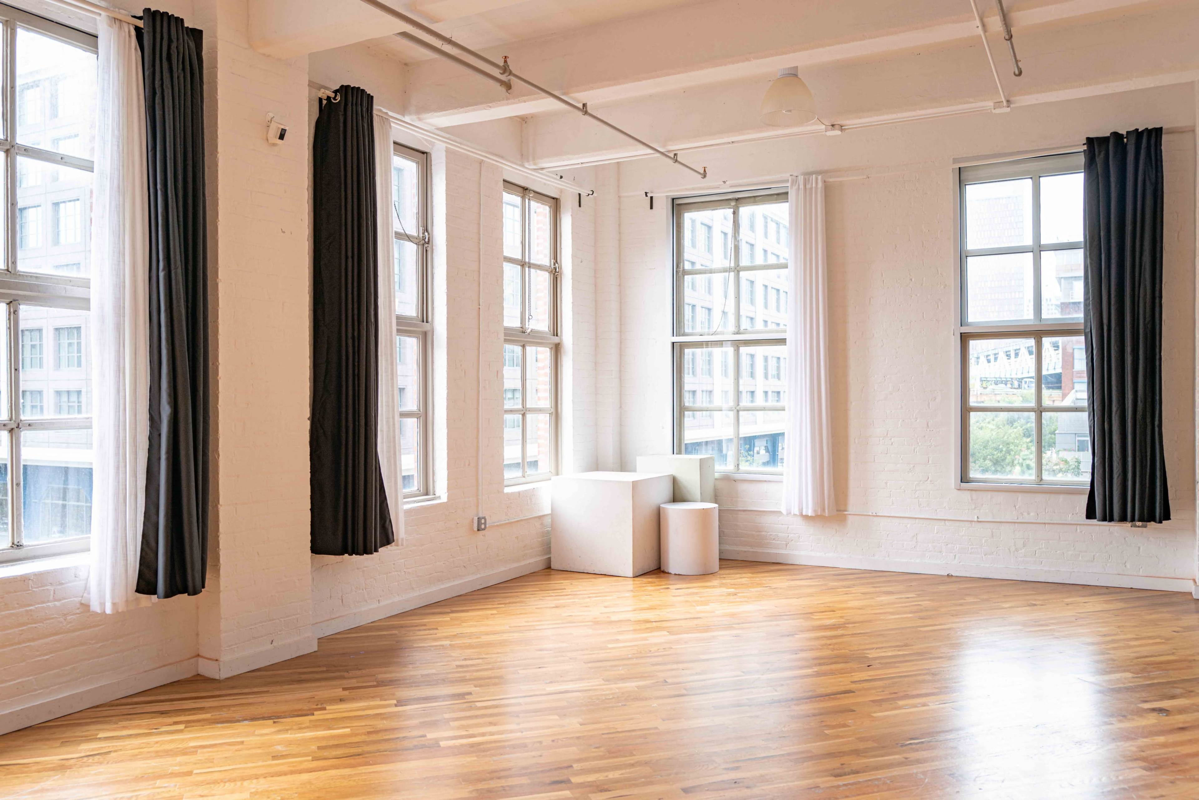 A bright, empty room with wooden flooring, large windows, and white walls.
