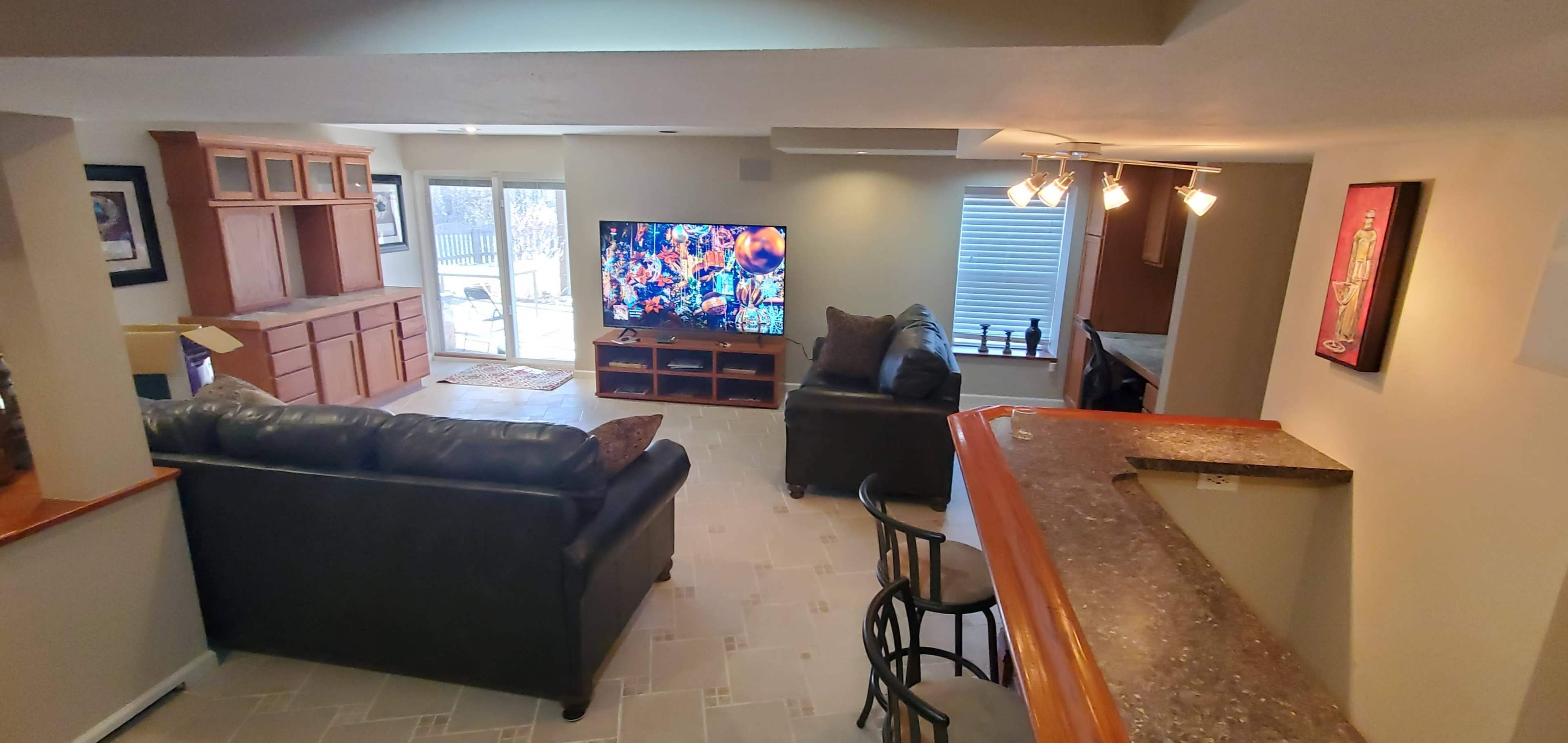 A spacious living area features a television, seating, and a bar counter, with large windows allowing natural light.