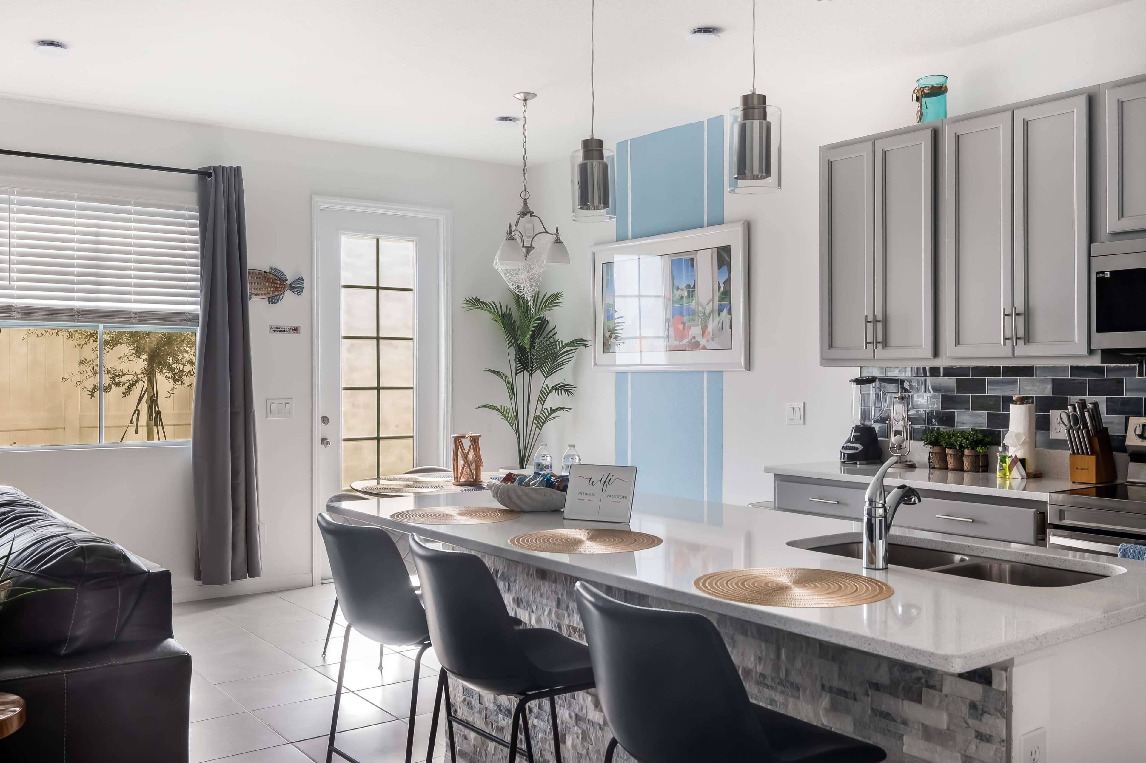 A modern kitchen features a central island with bar stools, light gray cabinets, and a door leading to an outdoor area.