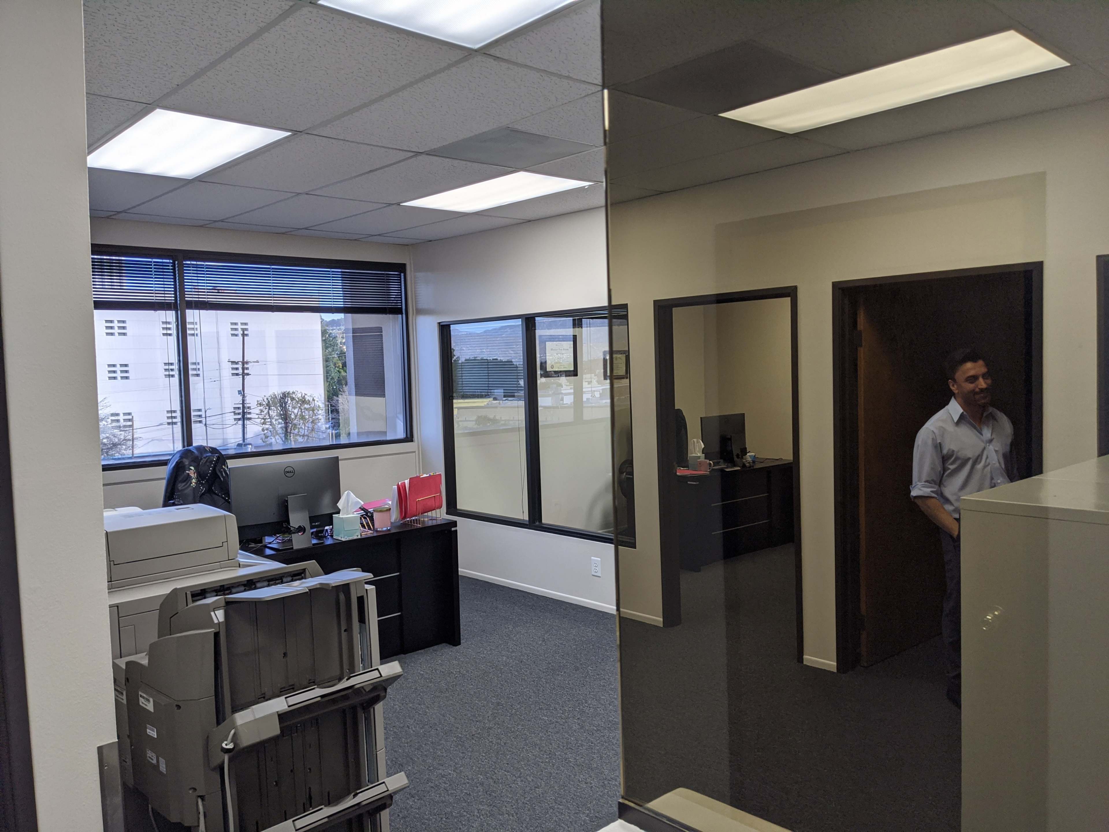An office space with cubicles, a printer, and a man standing in a doorway.