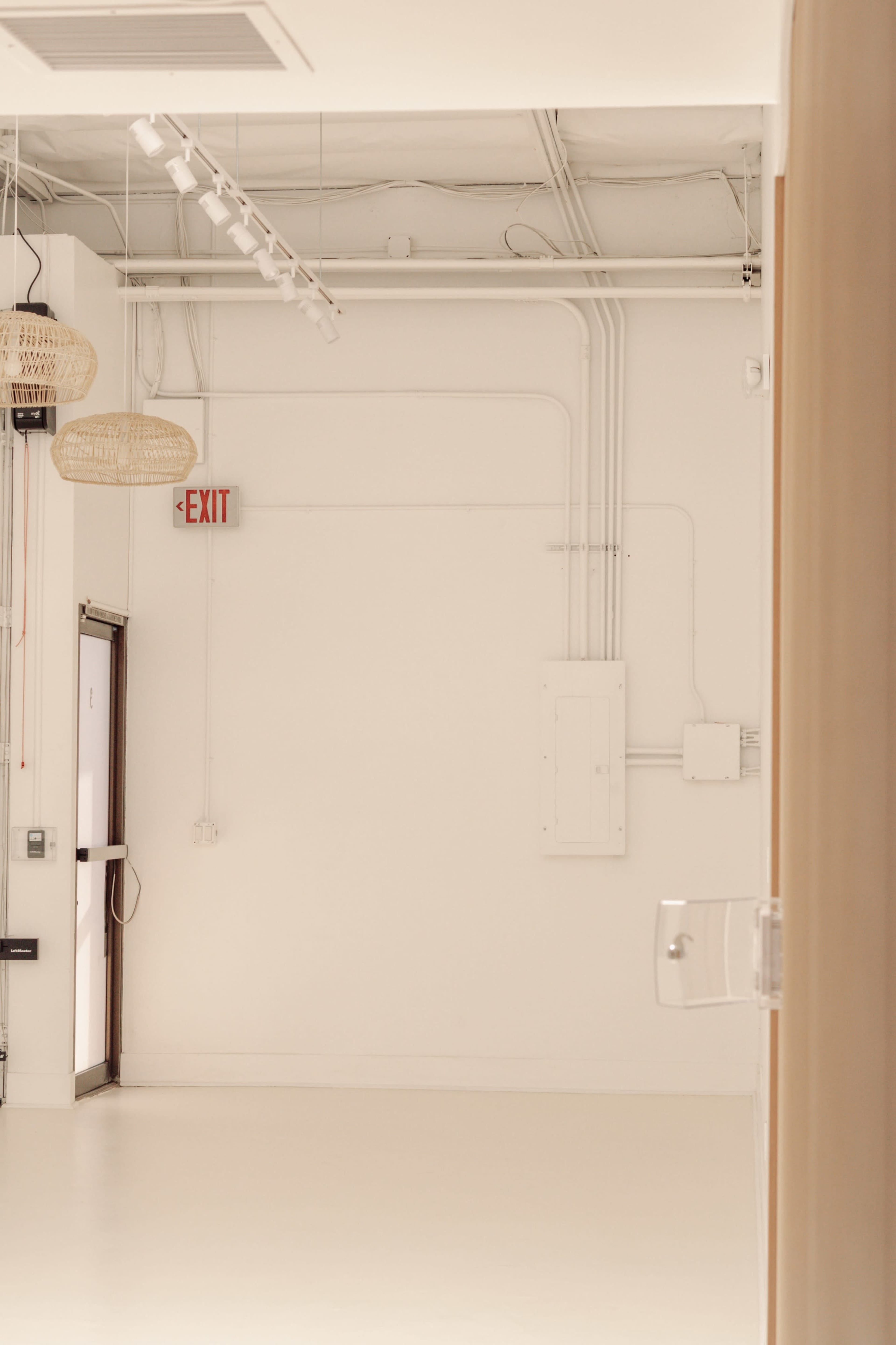 The image shows a spacious, empty room with white walls and a door leading to an exit.