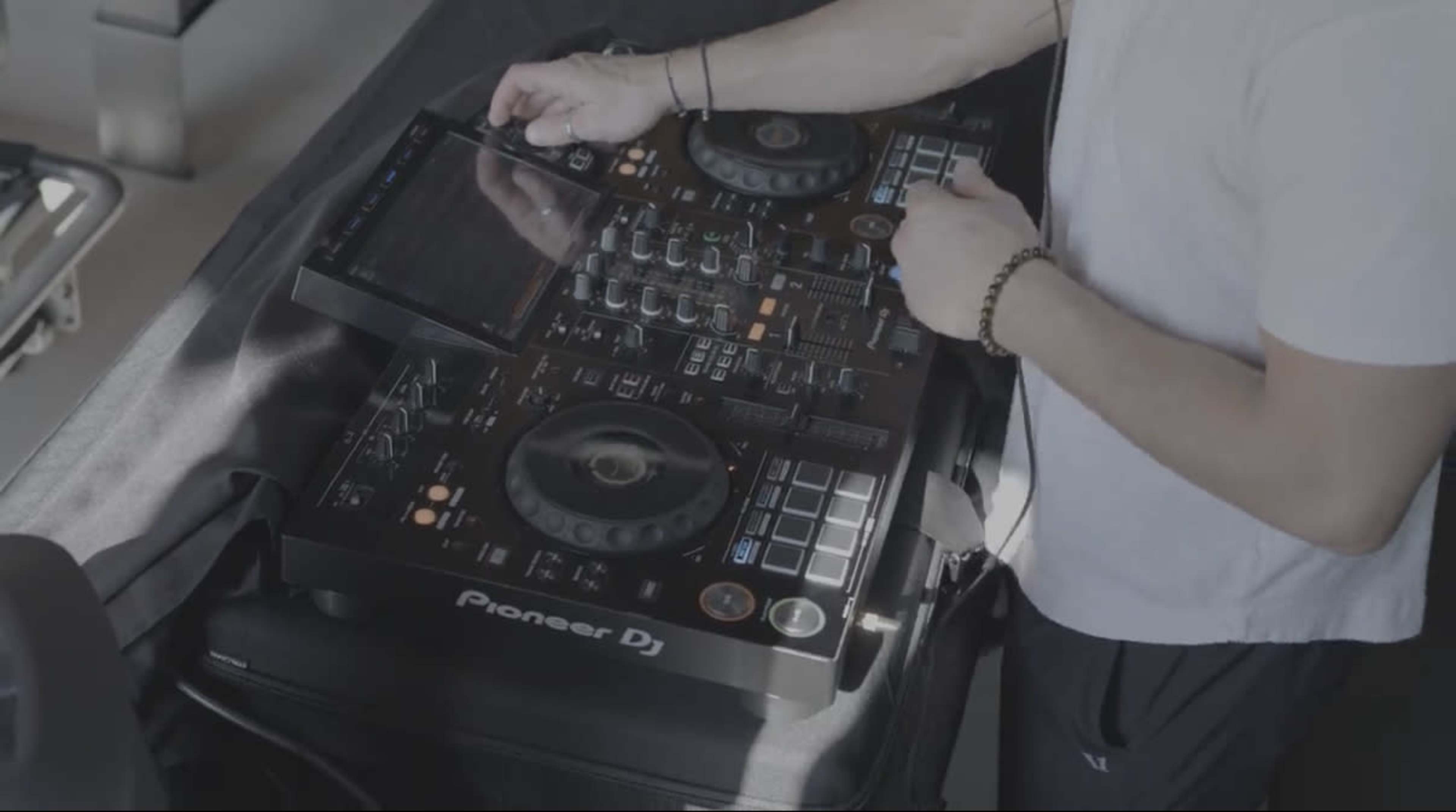 A person is using a Pioneer DJ controller while standing at a table.