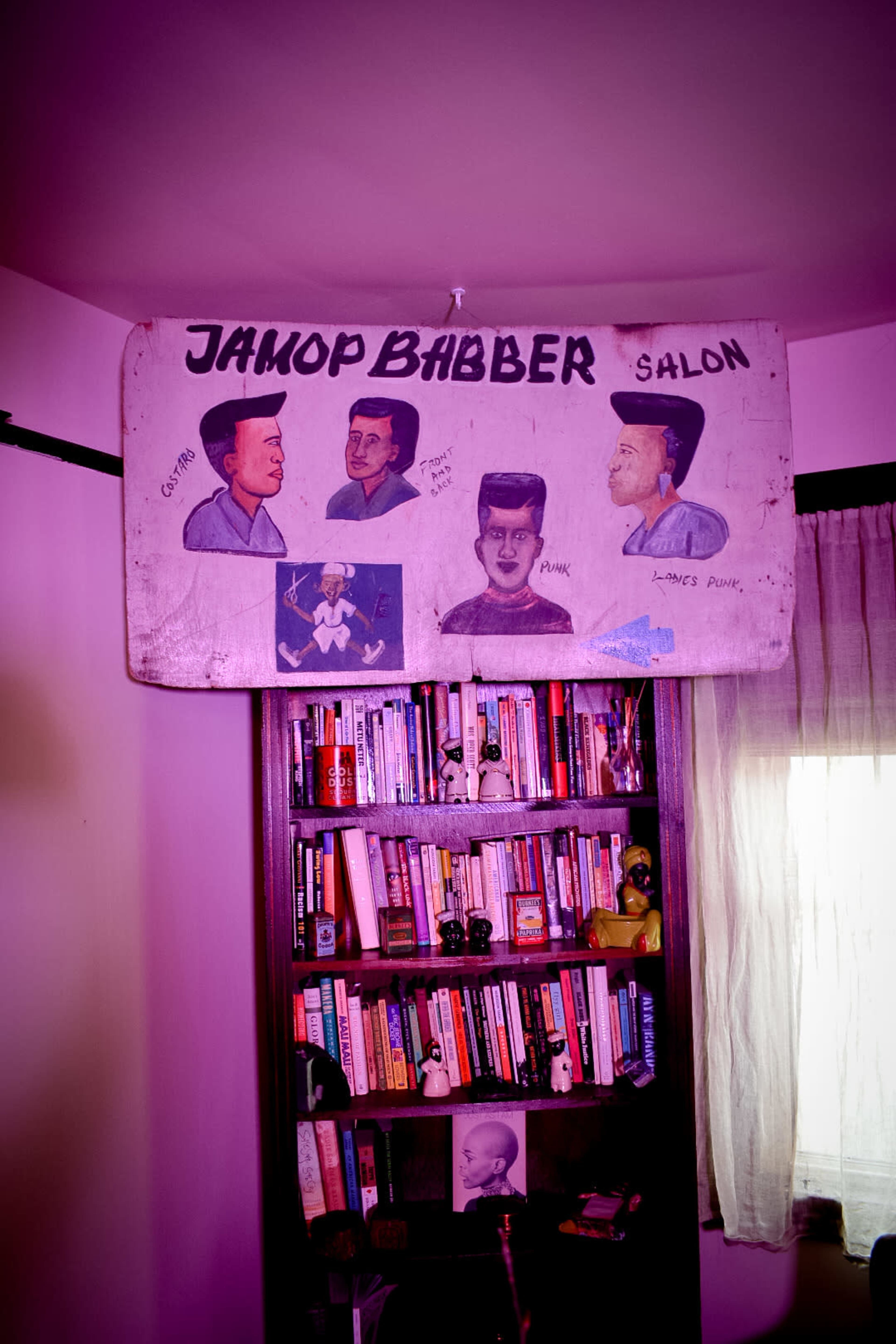 A wooden sign reading "Jainop Babber Salon" is displayed above a bookshelf filled with books, featuring illustrations of four hairstyles.