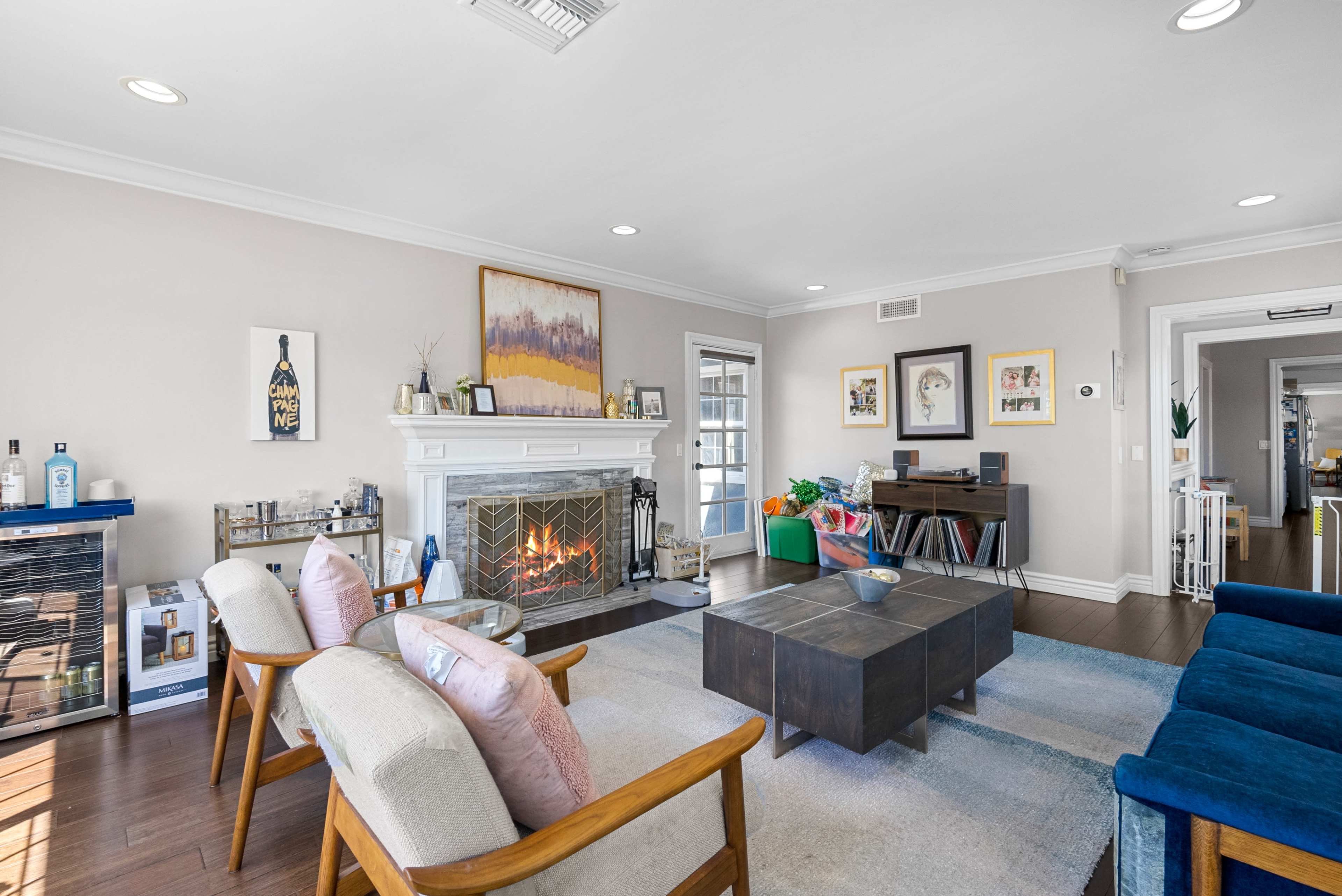 The living room features a fireplace, a coffee table, armchairs, and a bookshelf against light-colored walls.