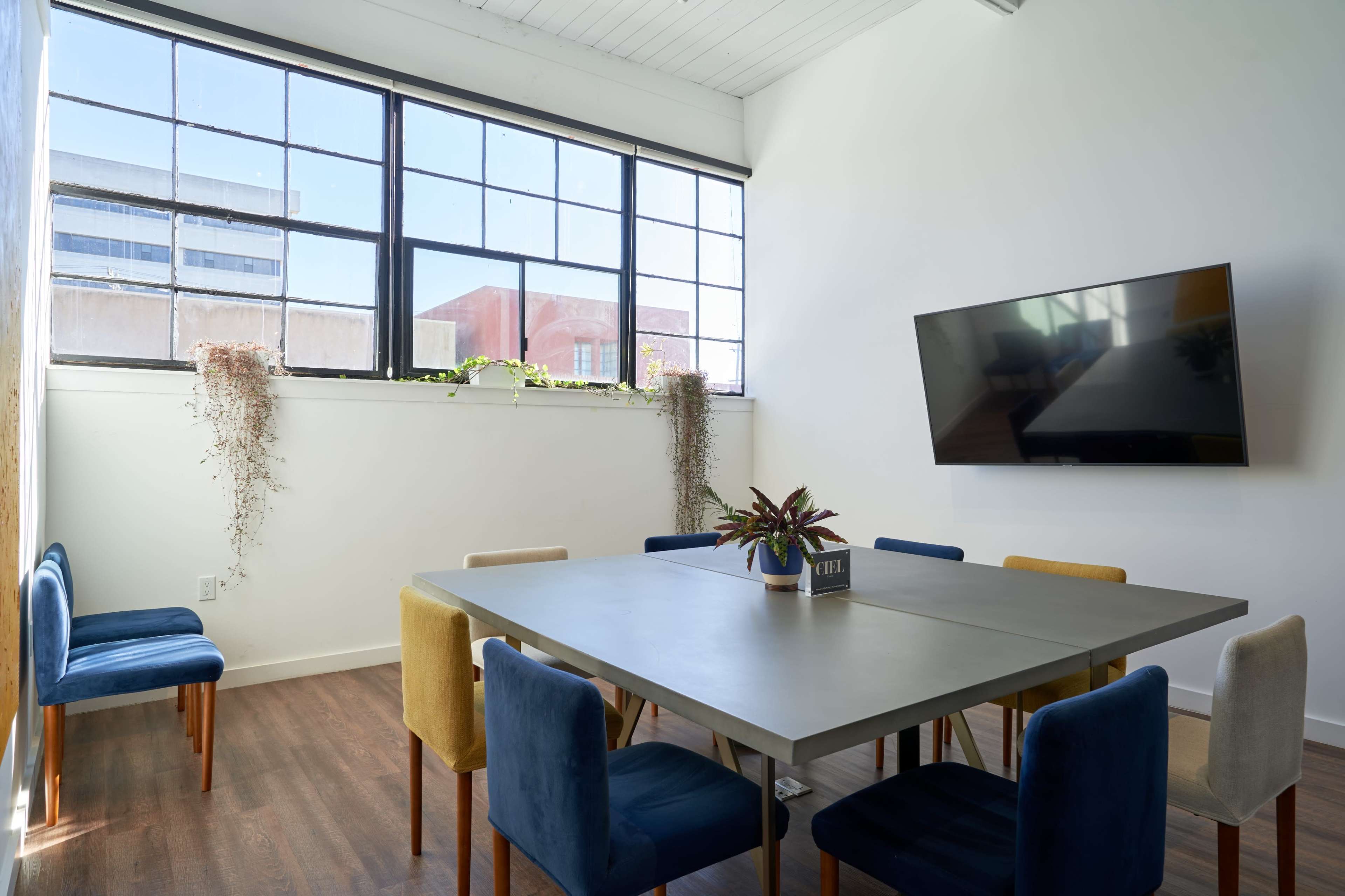 A bright meeting room with a large table surrounded by colorful chairs and a wall-mounted television.