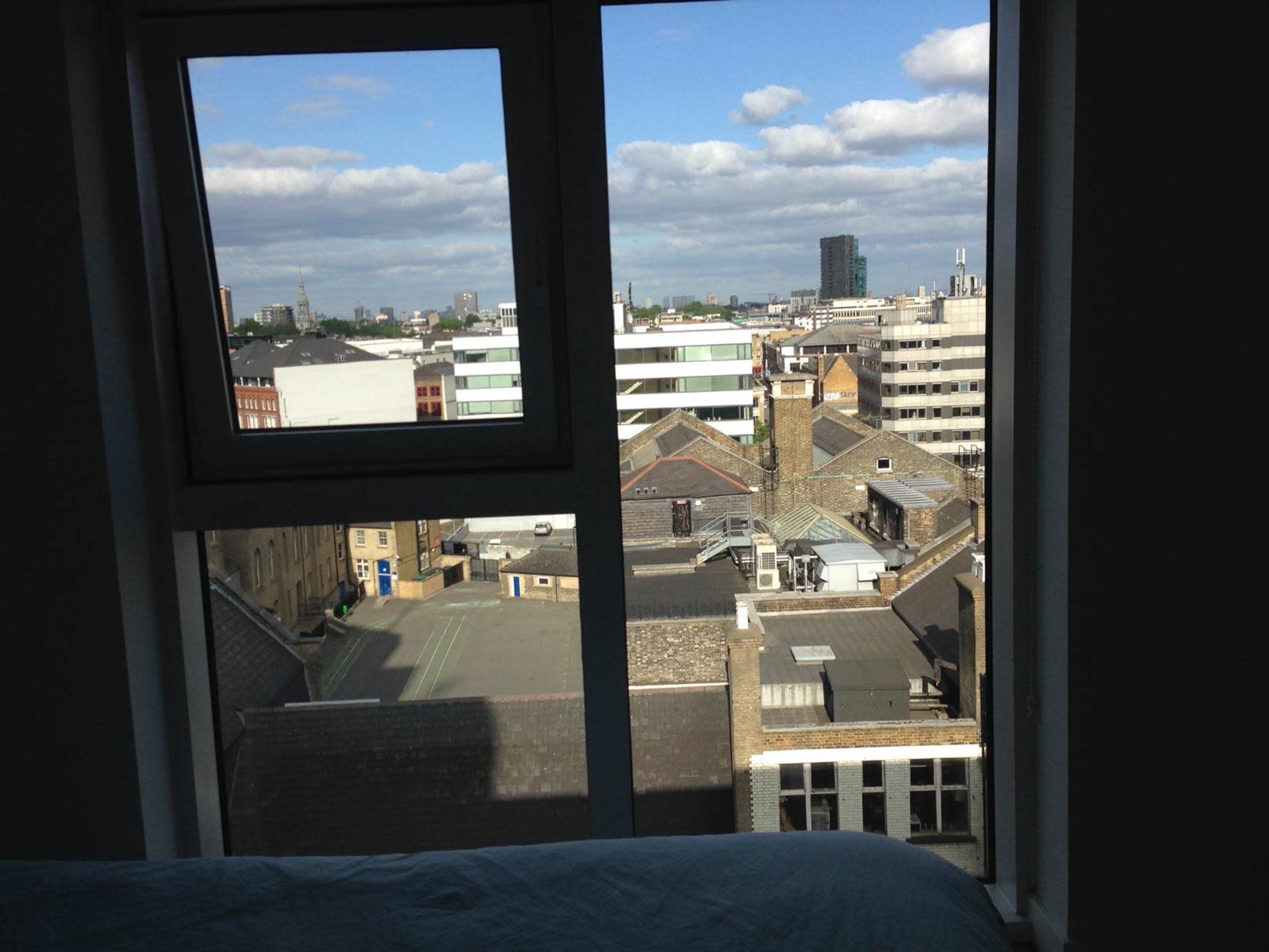 The image shows a cityscape view from a window, featuring a mix of buildings and rooftops under a partly cloudy sky.
