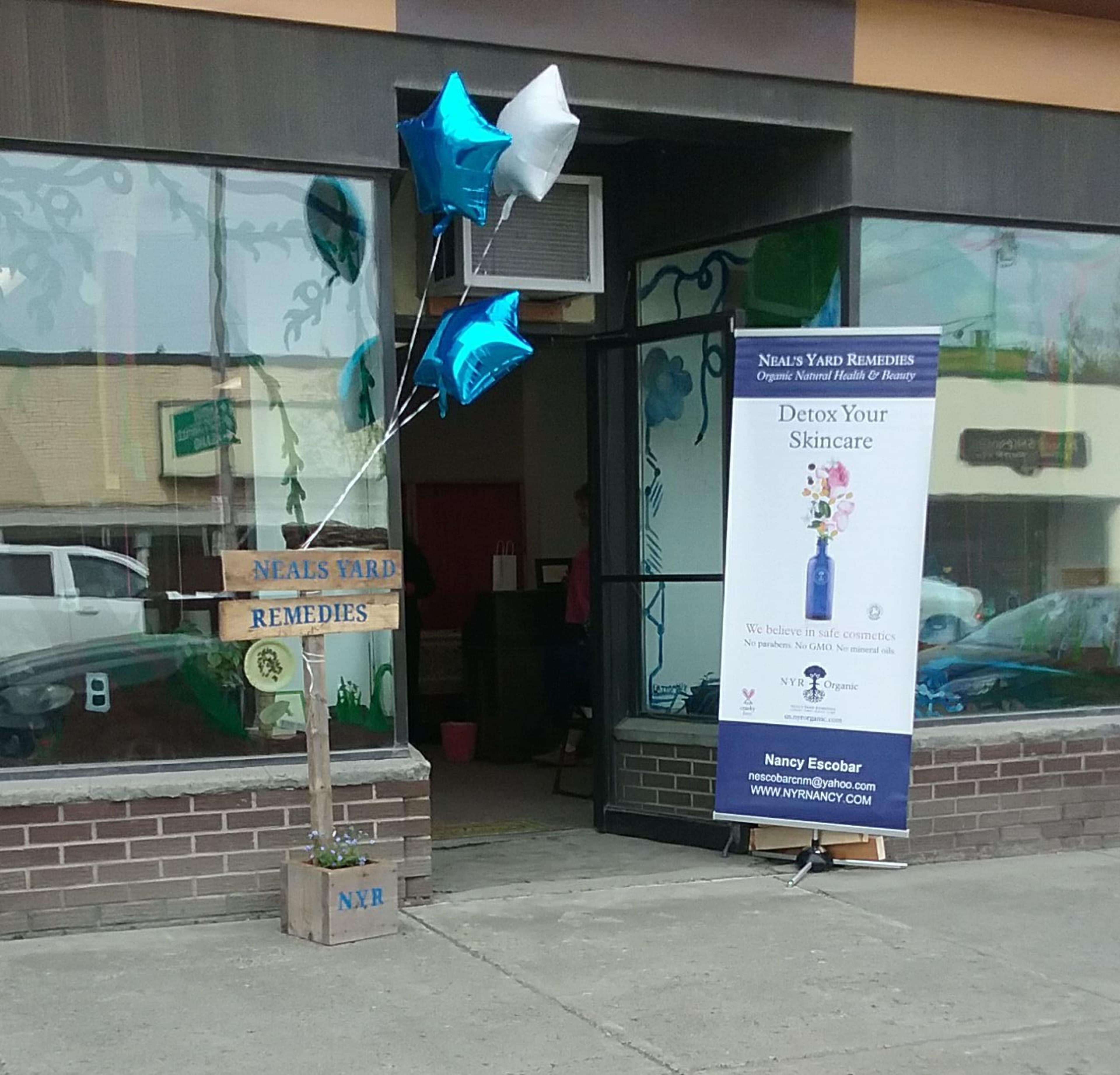 A storefront with a wooden sign for "Neal's Yard Remedies" and a banner advertising skincare products, accompanied by blue balloons.