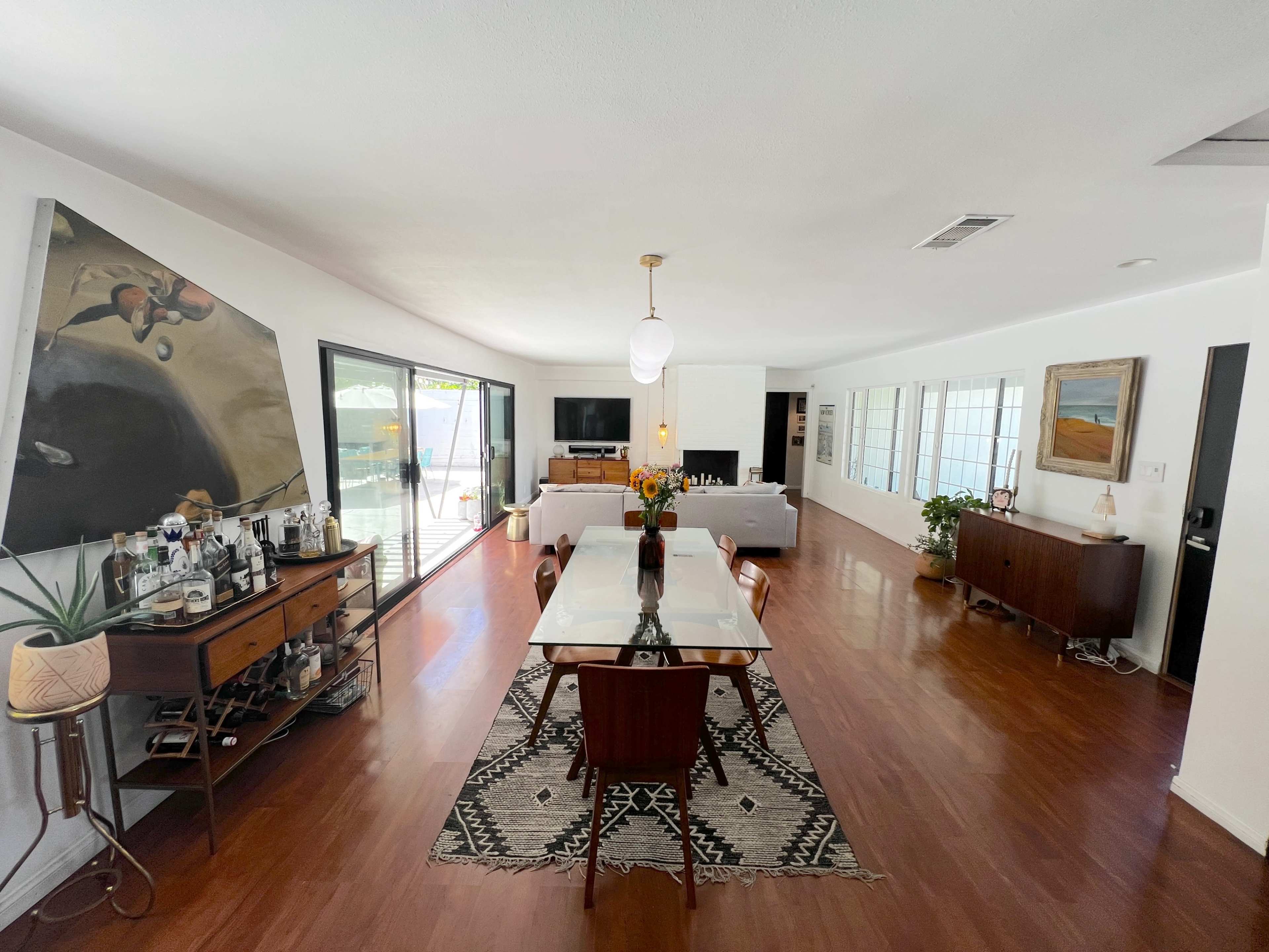 The image shows a modern, open-concept living and dining area with a long table, seating for six, and large windows allowing natural light to fill the space.