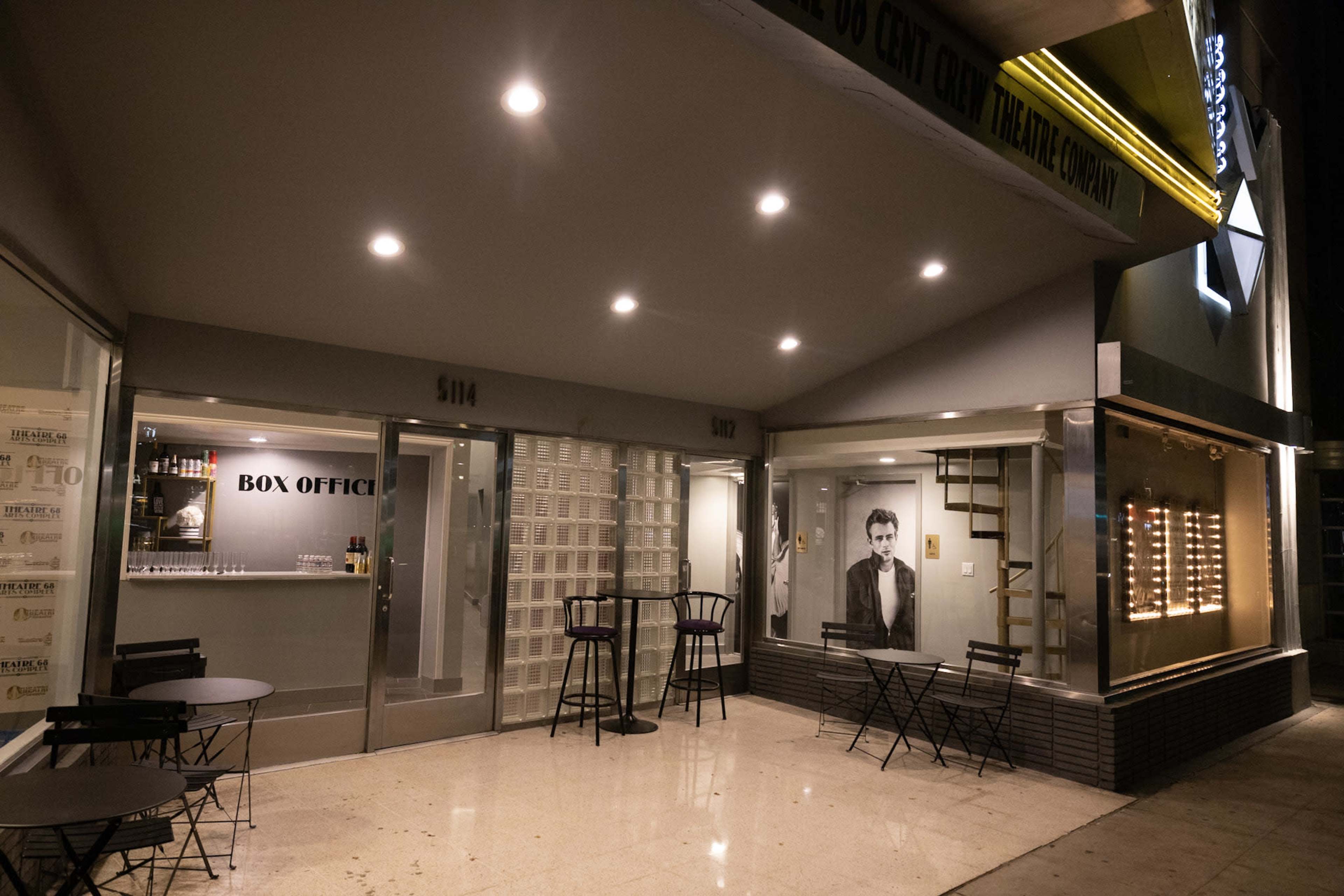 A theater box office with seating outside and a large black-and-white portrait of a man on the wall.