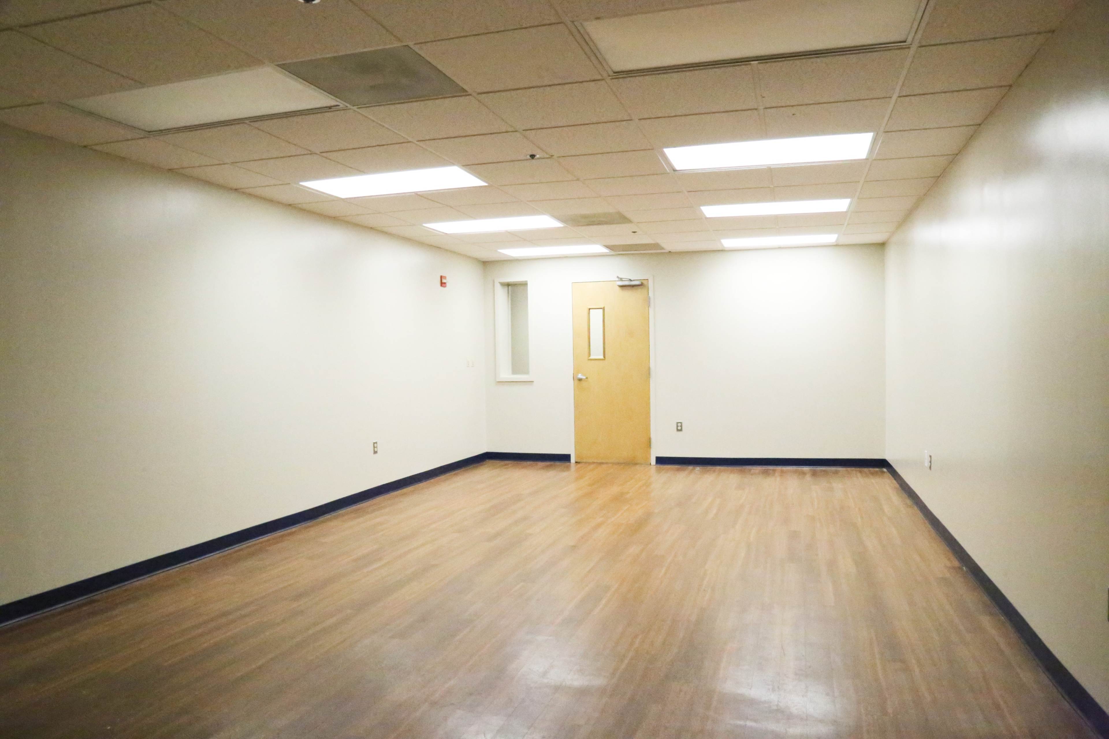 An empty room with a wooden floor, beige walls, and a single door on one side.