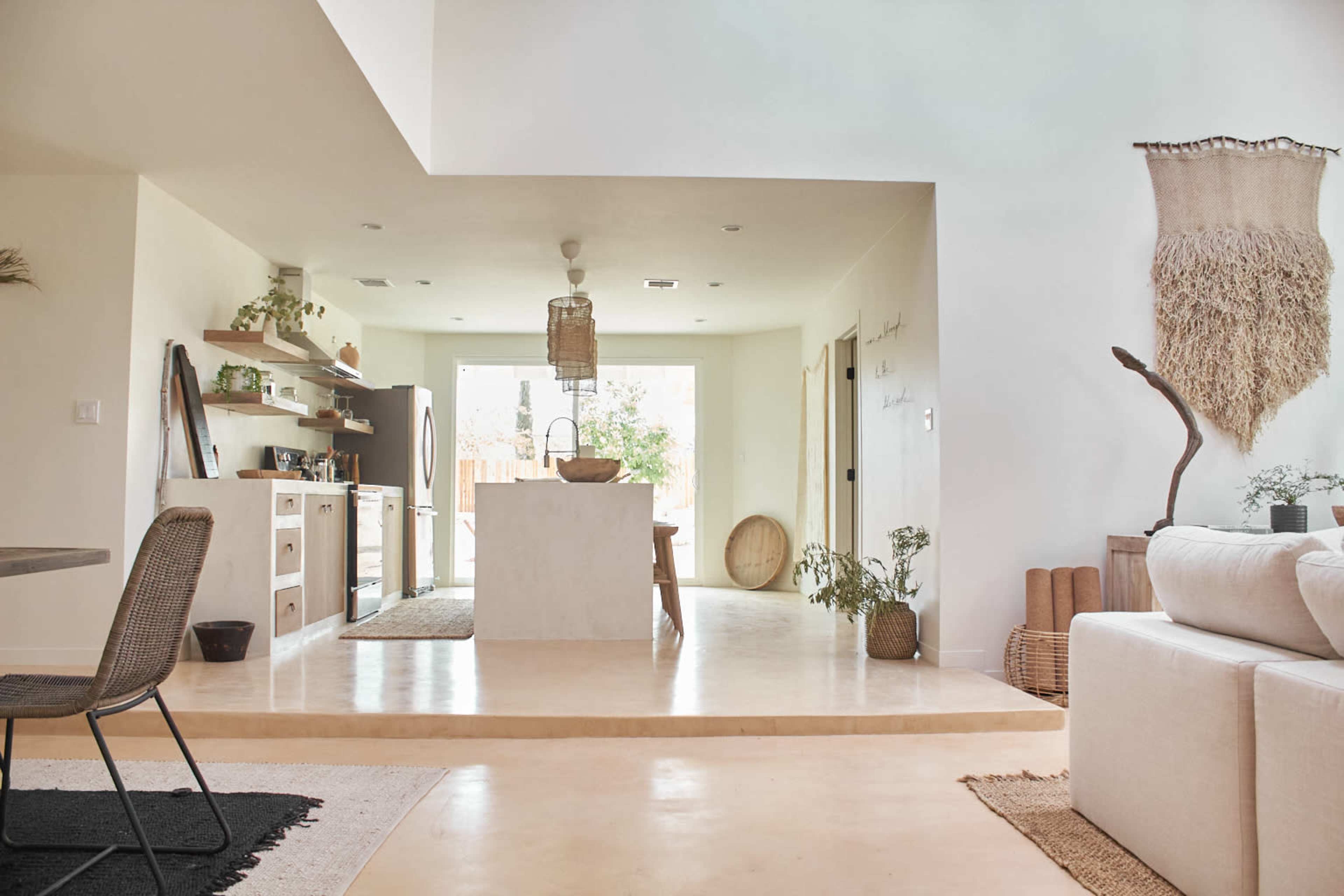 The image shows a modern, open-concept living space with a kitchen, dining area, and seating area adorned with neutral tones and minimalist decor.