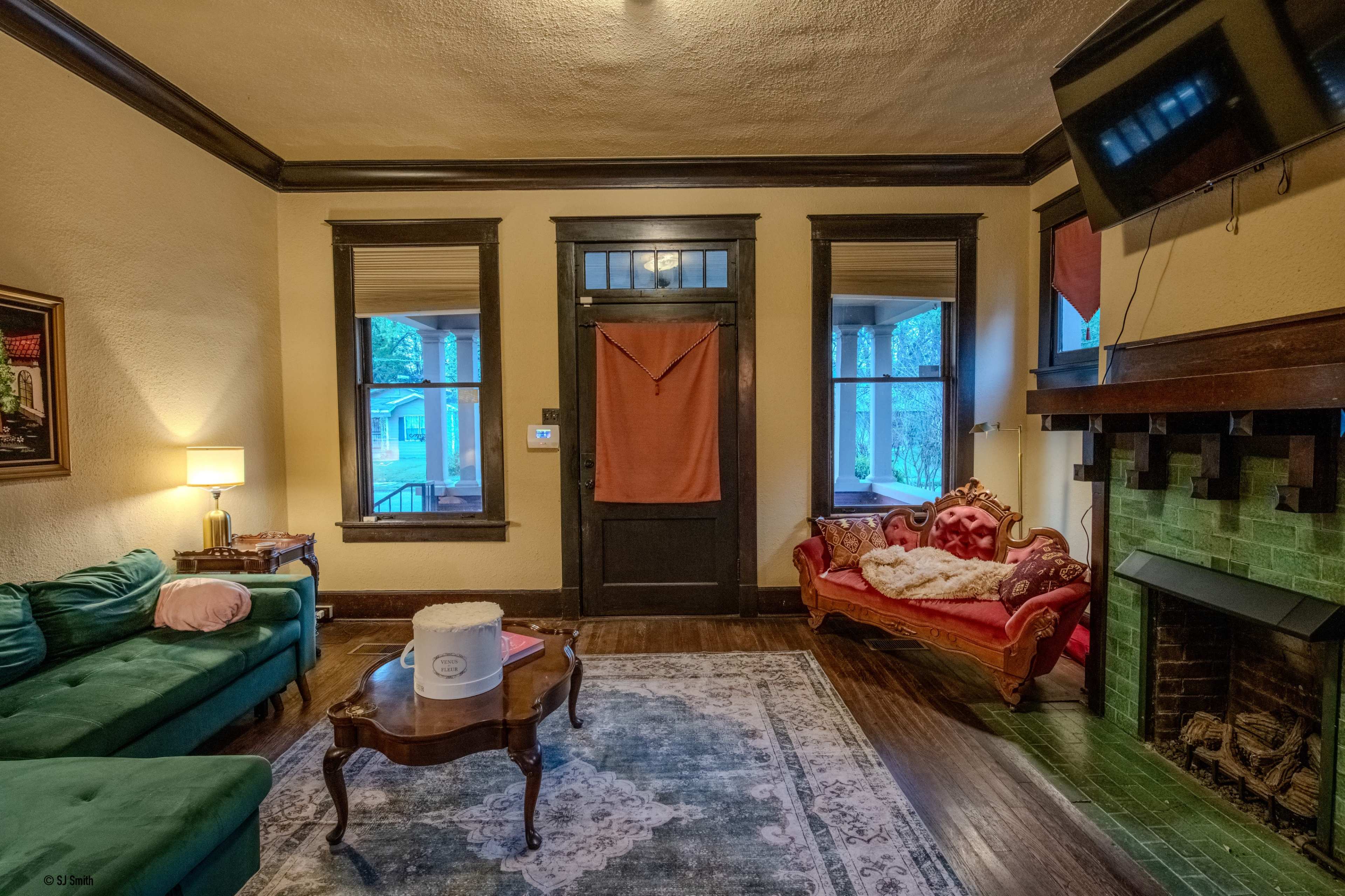 A living room featuring a green sofa, a red Victorian-style loveseat, a wooden coffee table, and a fireplace with a green tile surround.
