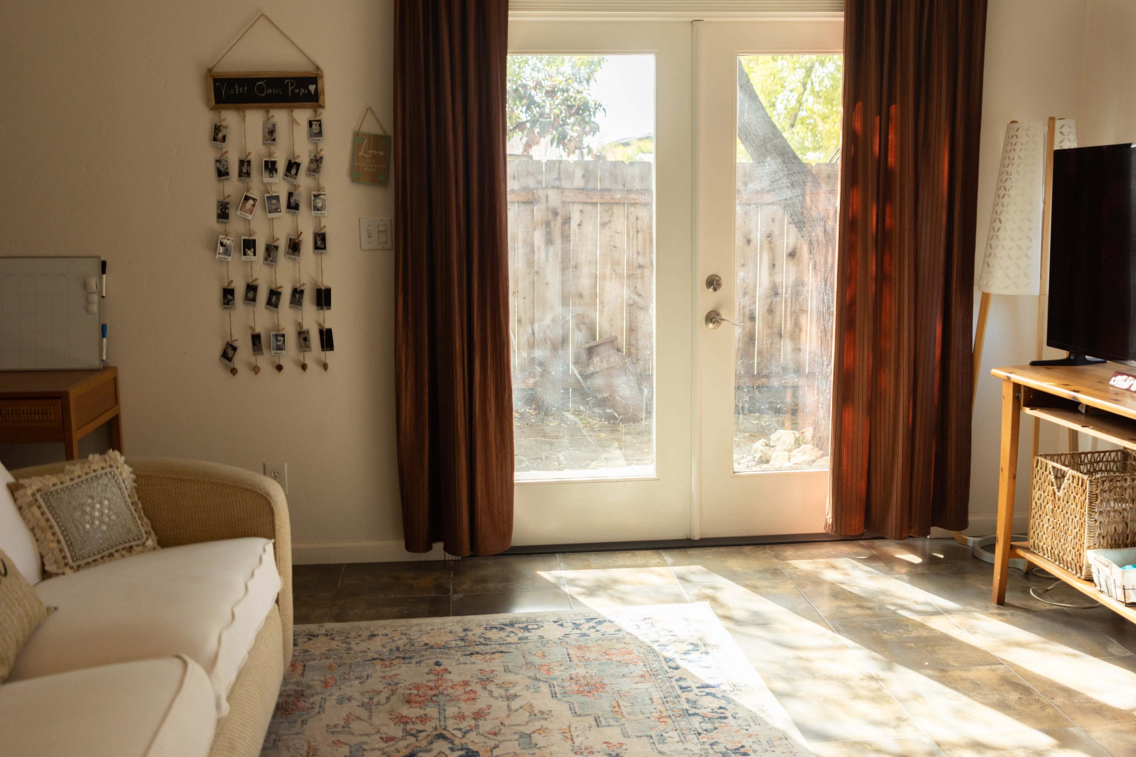 A cozy living room features a white couch, a wall-mounted photo display, and large glass doors leading to an outdoor area with a wooden fence.