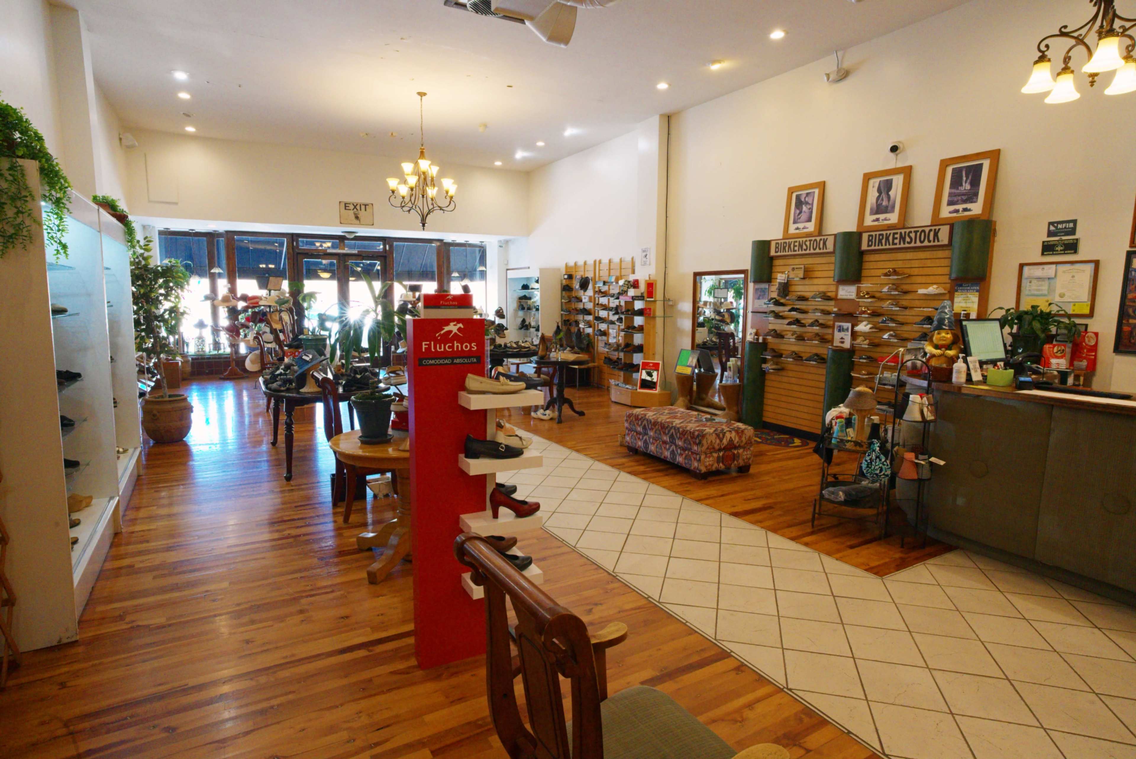 The image shows a retail space featuring wooden flooring, shoe displays on the walls, and a central seating area with a patterned sofa.