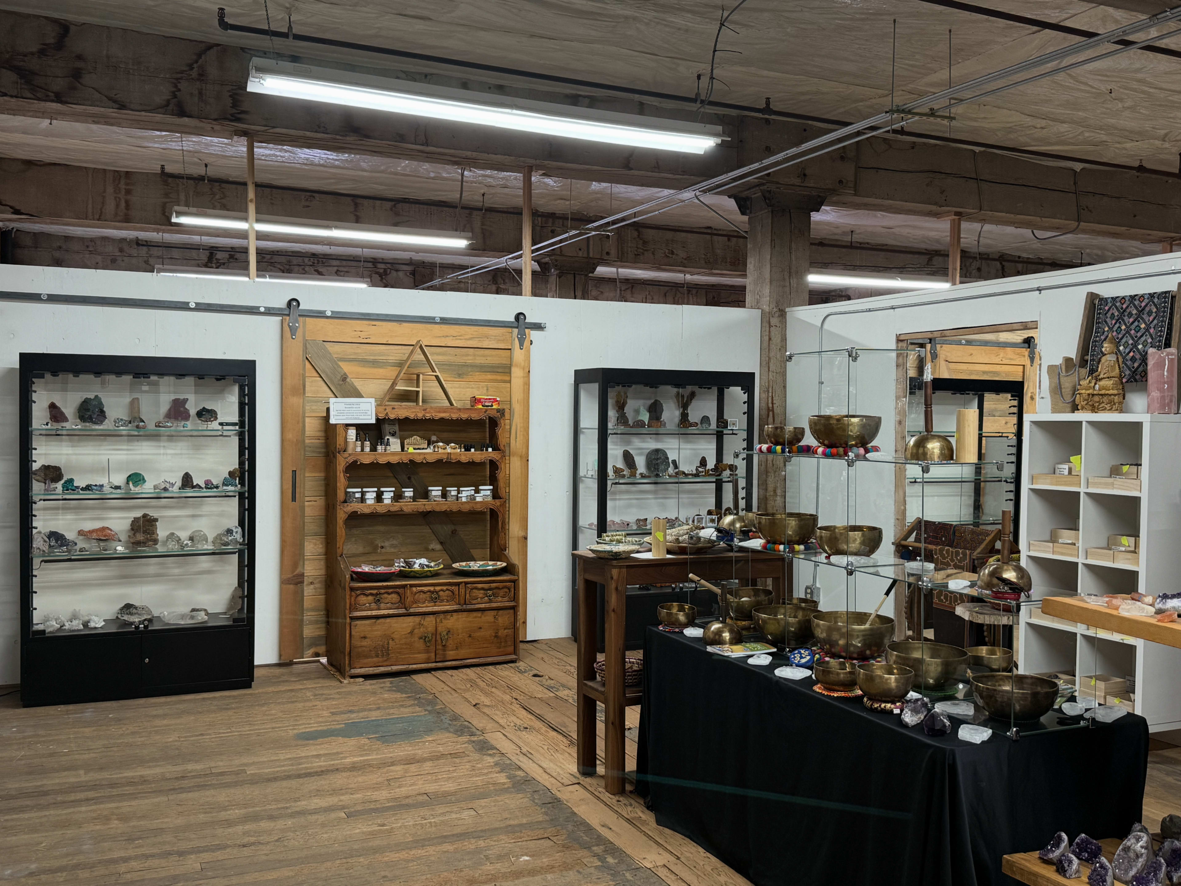 The image shows an interior space filled with glass display cases showcasing various items, wooden shelves stocked with products, and tables with bowls and crystals.