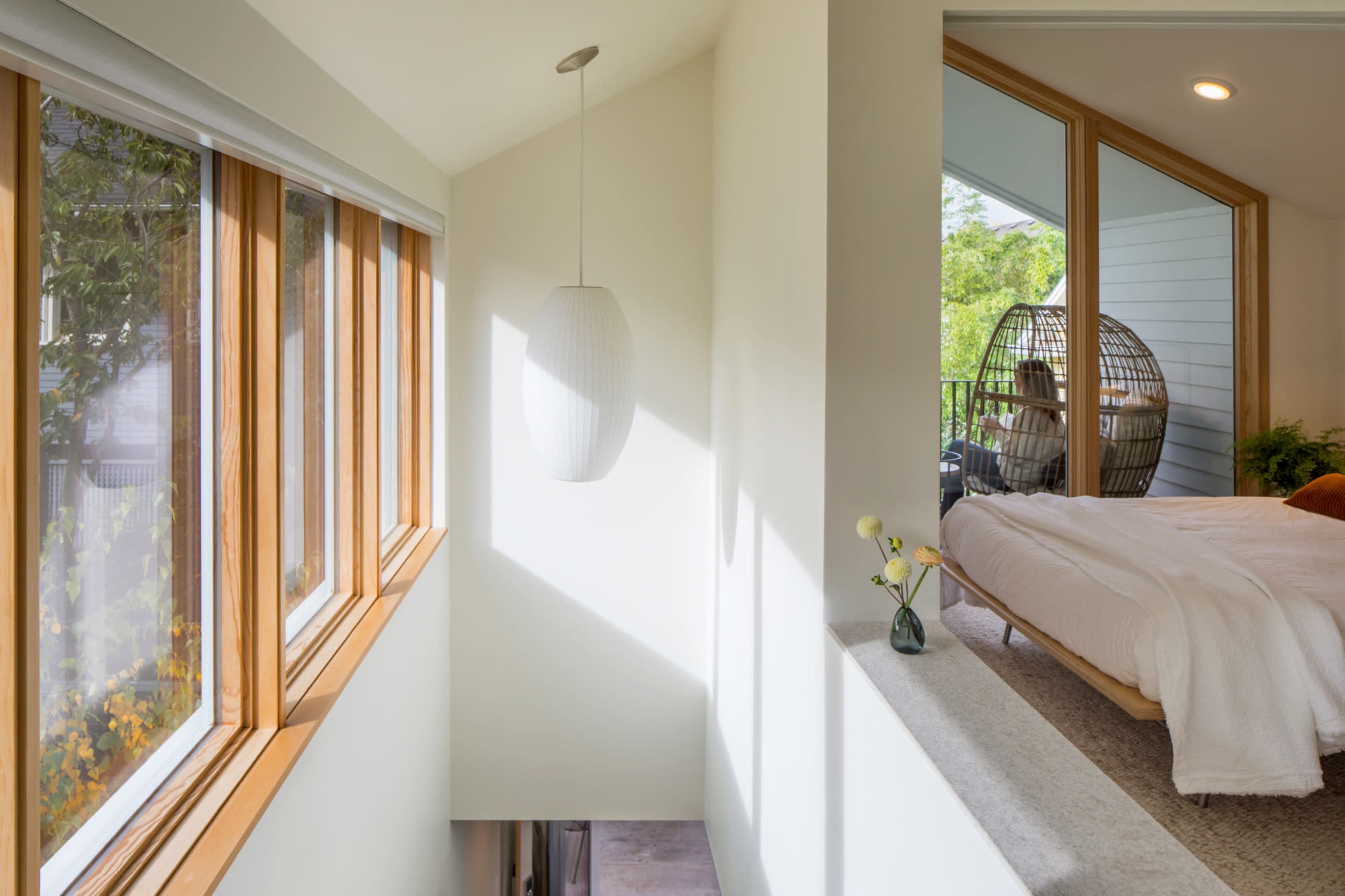 A bright, modern interior with large windows, a hanging light fixture, and a cozy seating area featuring a bed and a hanging chair.