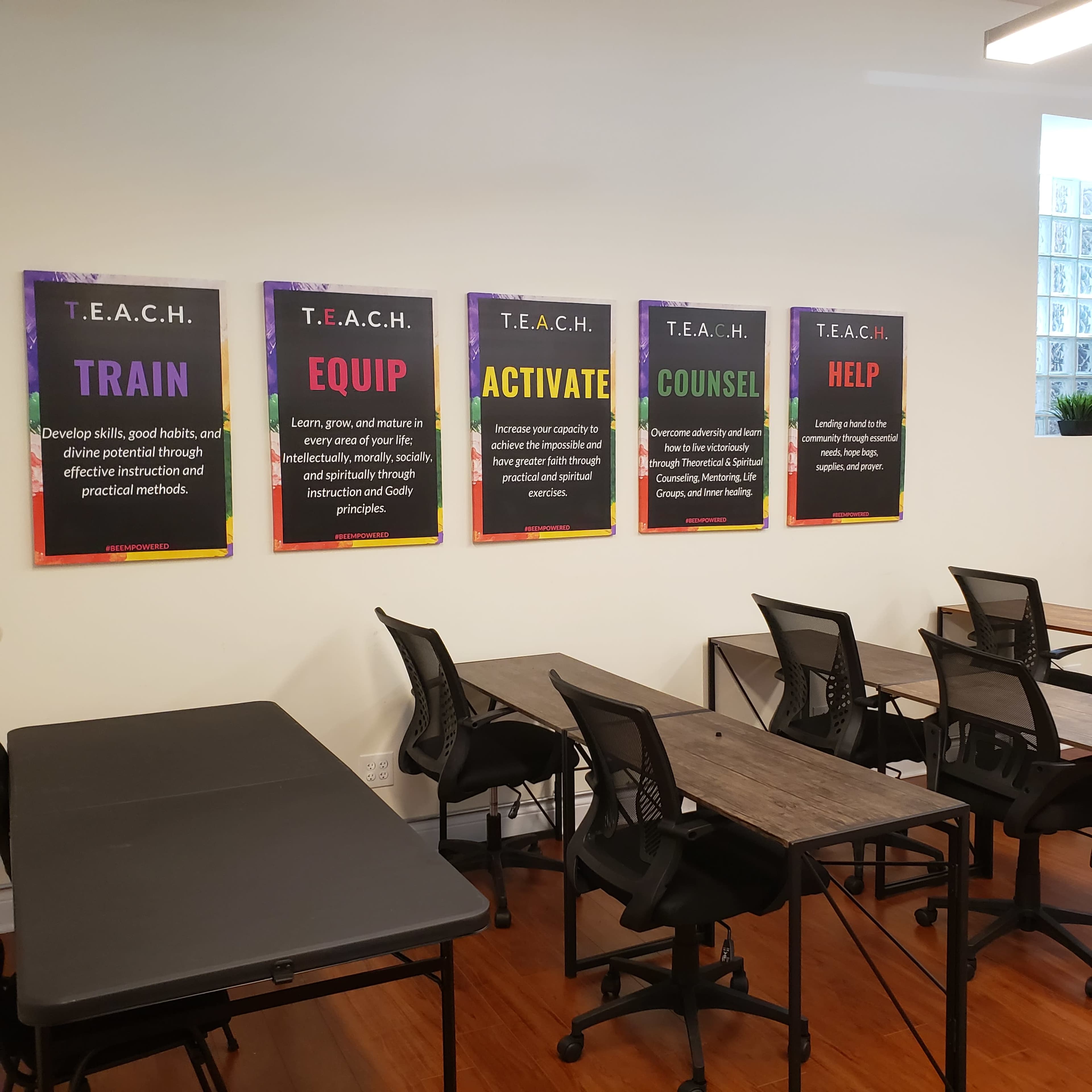 A classroom setting features a wall with colorful posters displaying the T.E.A.C.H. principles: Train, Equip, Activate, Counsel, and Help, alongside empty desks and chairs.
