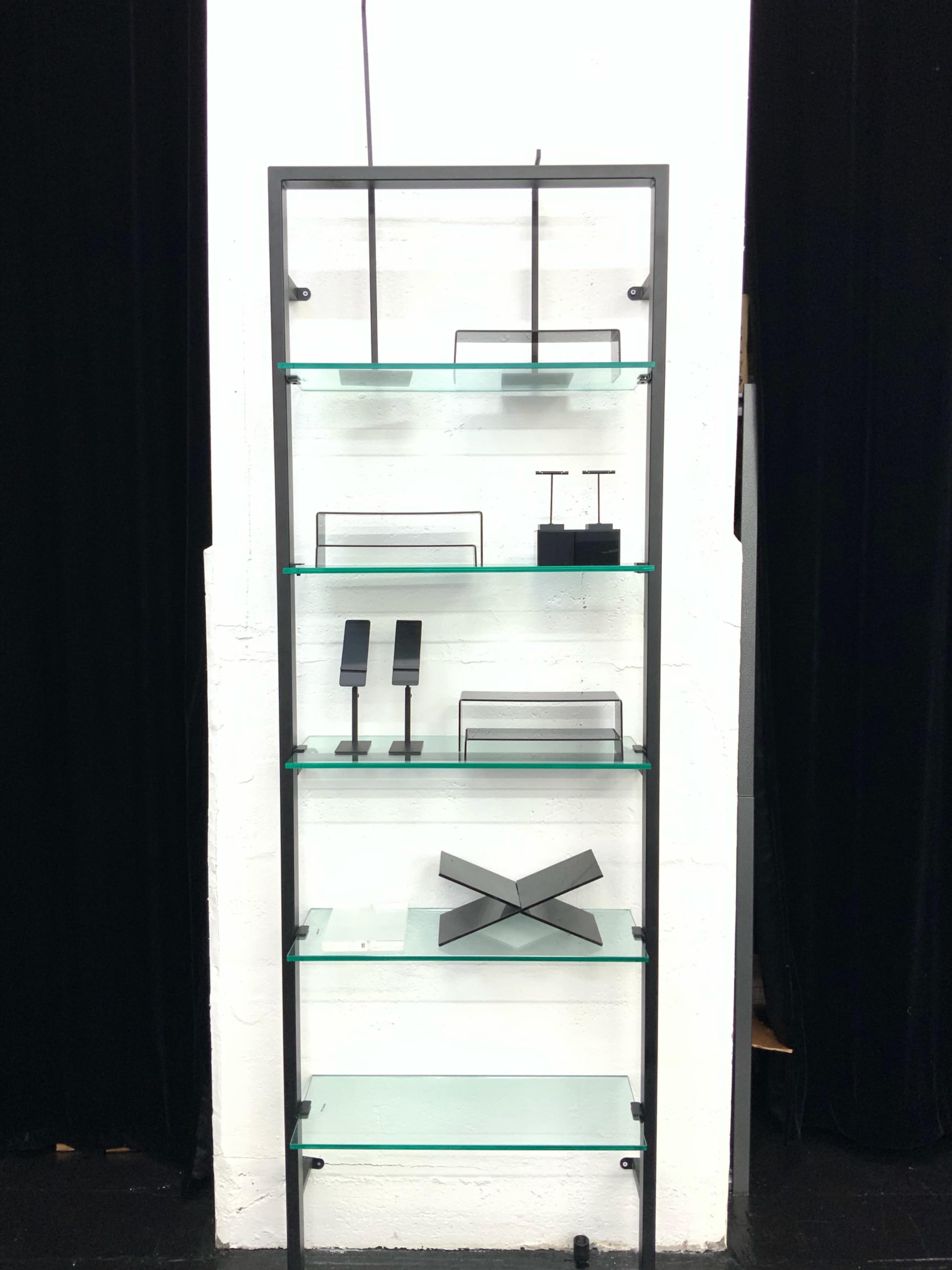The image shows a black metal shelving unit displaying various geometric metal and glass objects on transparent glass shelves.