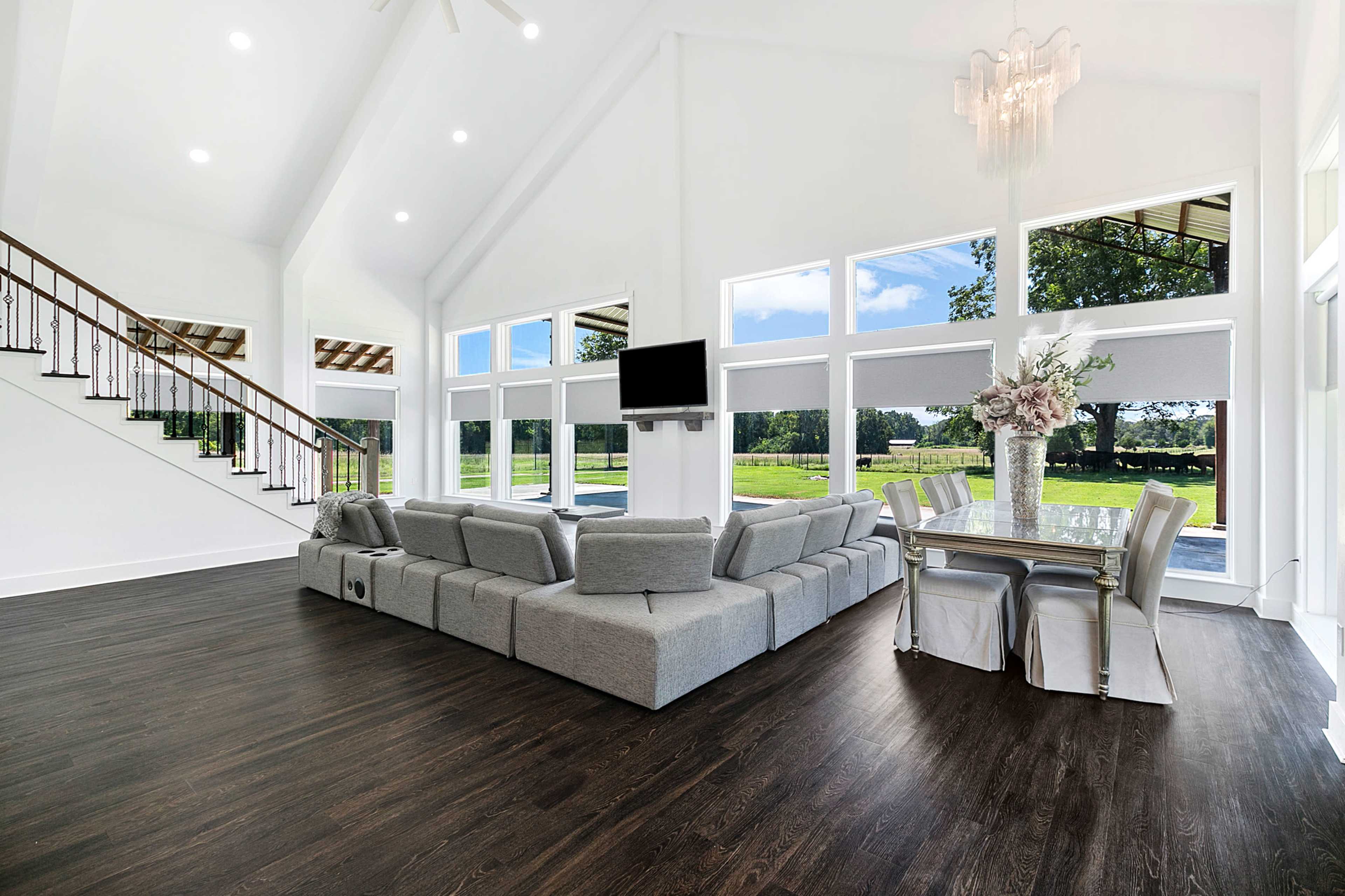 The scene features a spacious, modern living area with large windows, a sectional sofa, a dining table, and elegant decor.