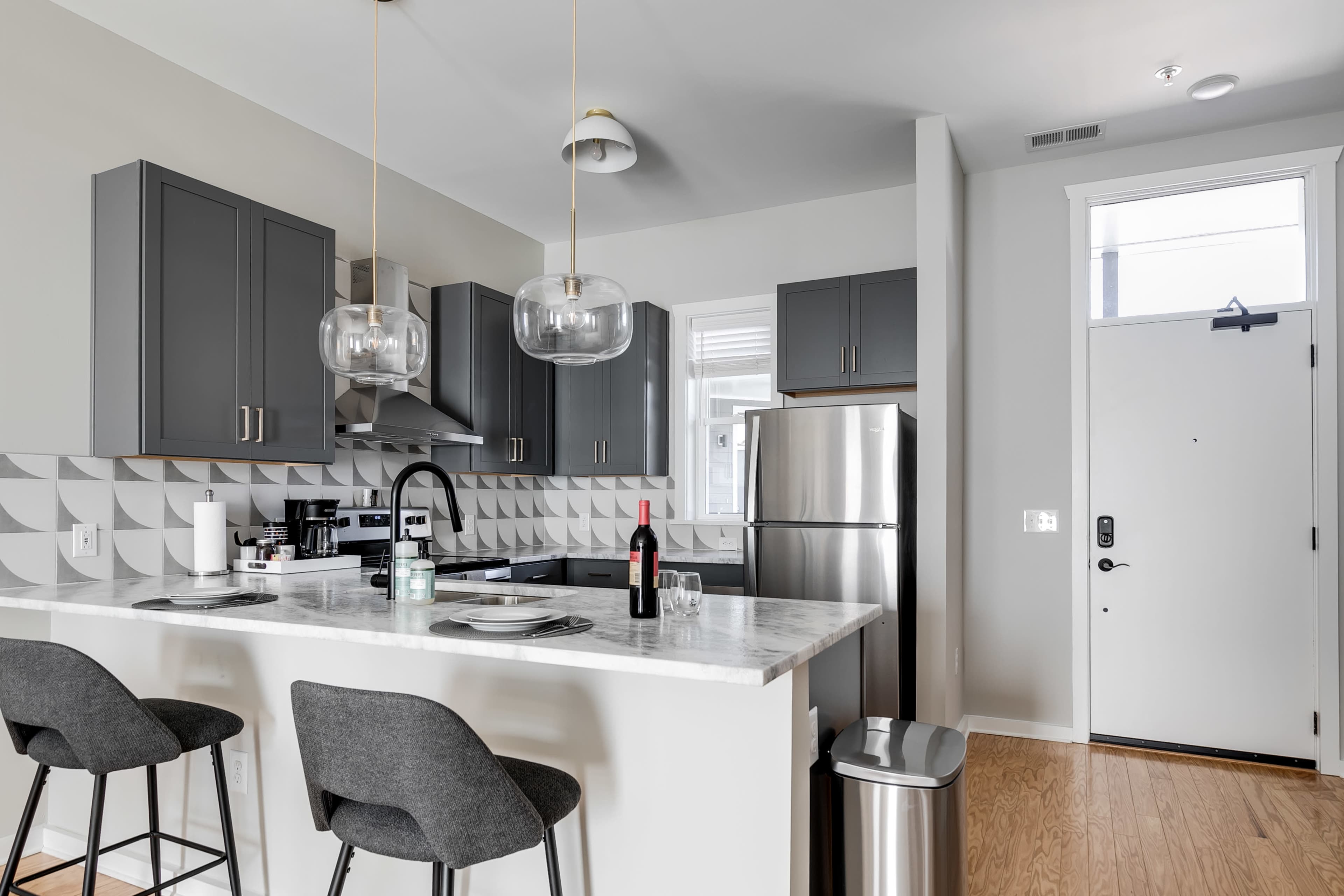 A modern kitchen features gray cabinetry, stainless steel appliances, a marble countertop, and two bar stools at the island.