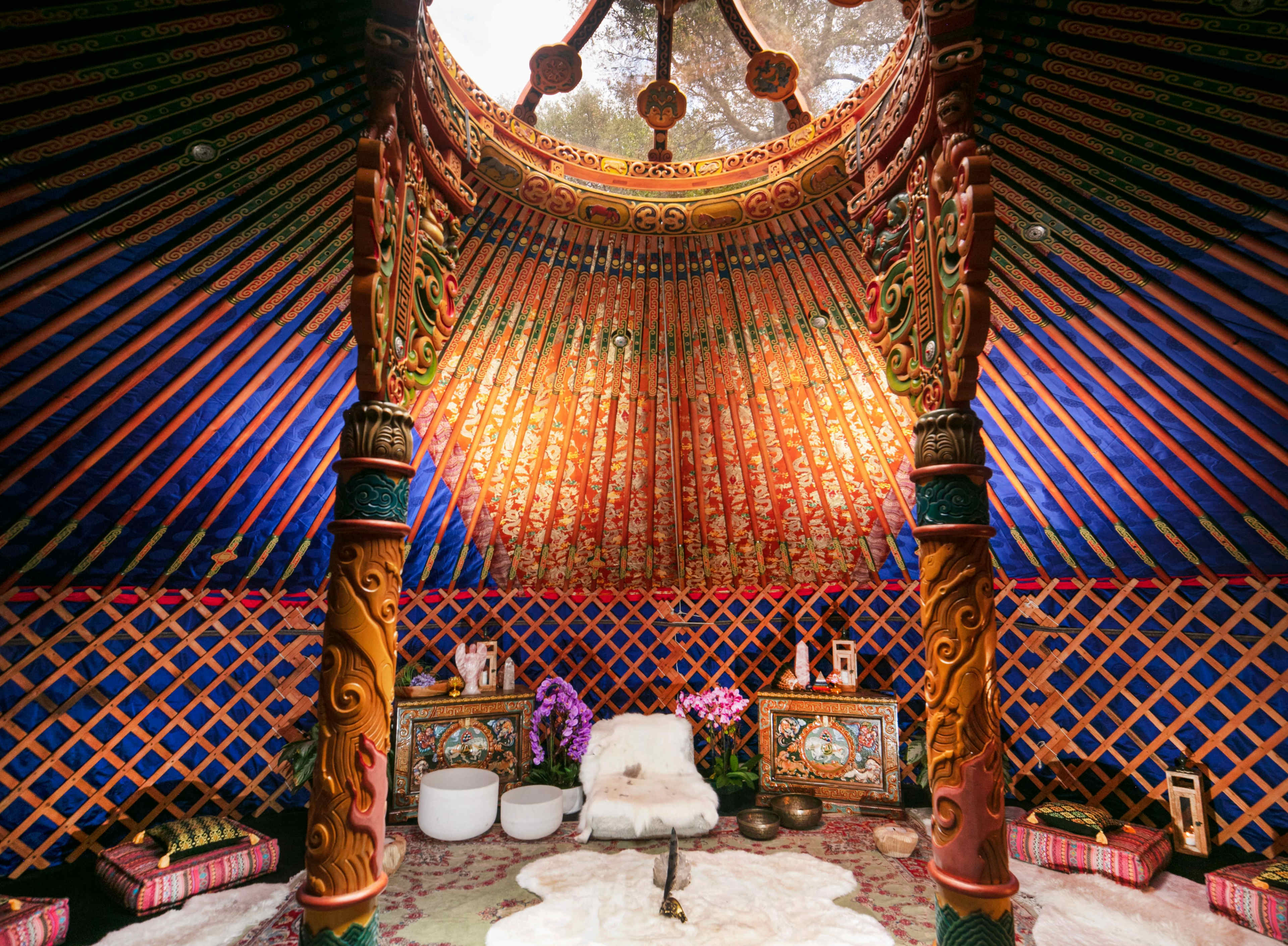 The interior of a traditional yurt featuring ornate, colorful decorations, a circular skylight, and plush seating arrangements.