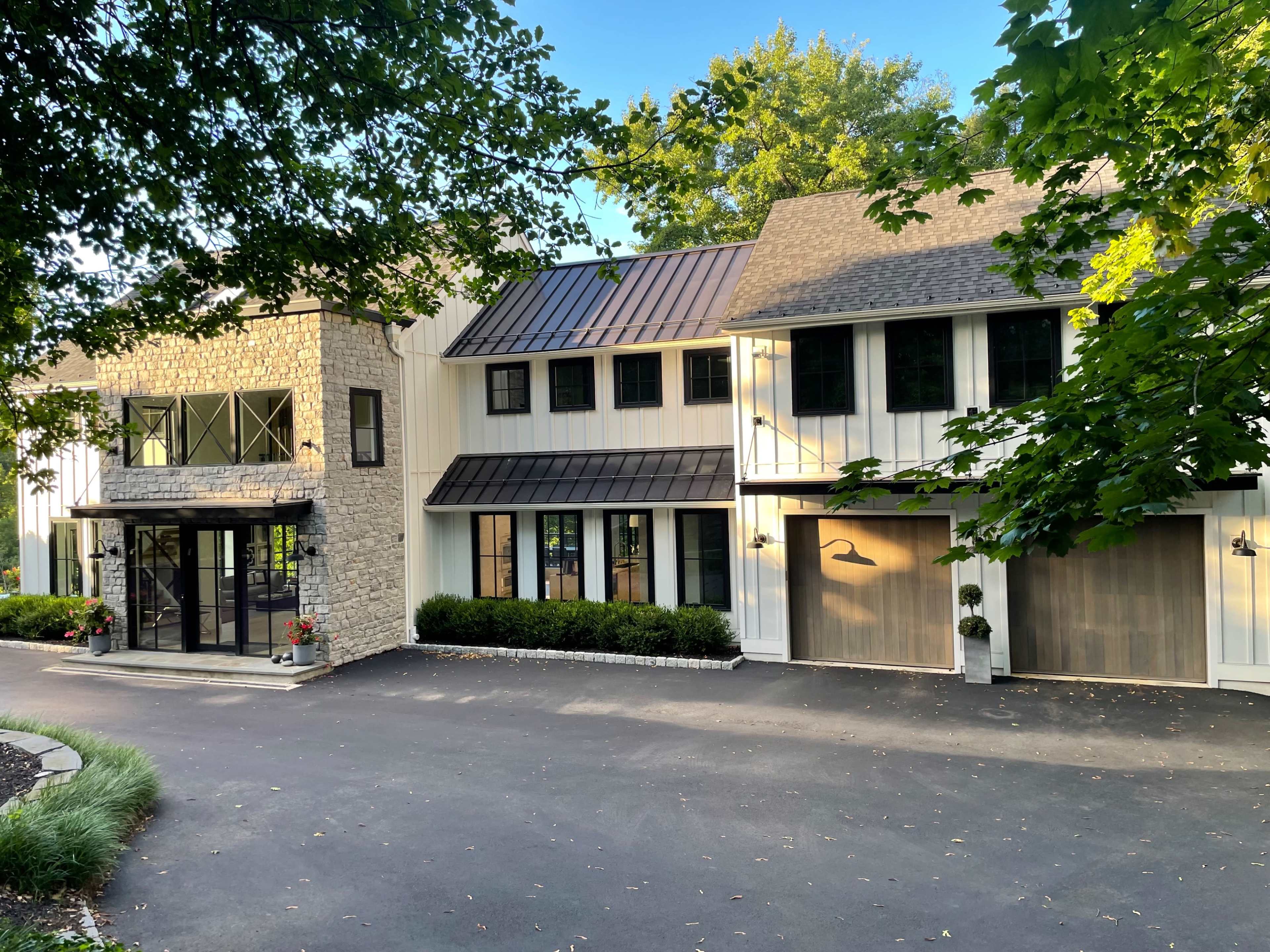 A modern two-story house with a mix of stone and wooden features, large windows, and a paved driveway.