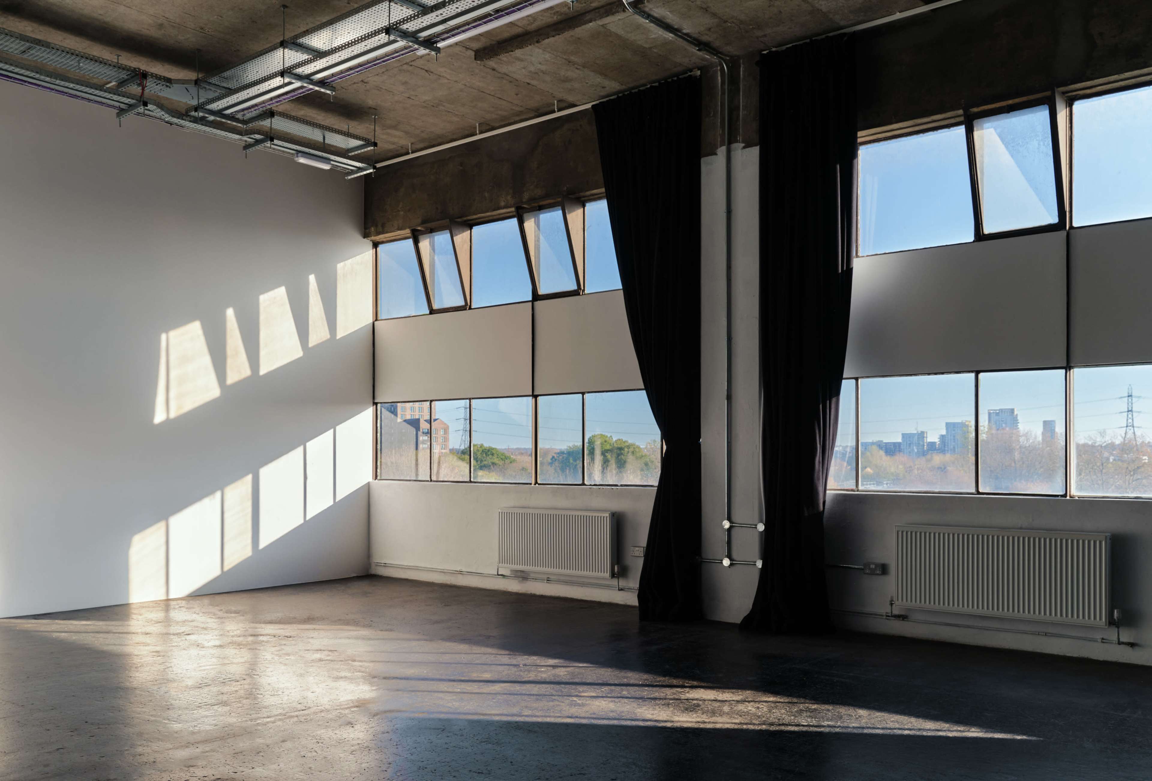 A modern, spacious room with large windows and natural light casting shadows on the floor.