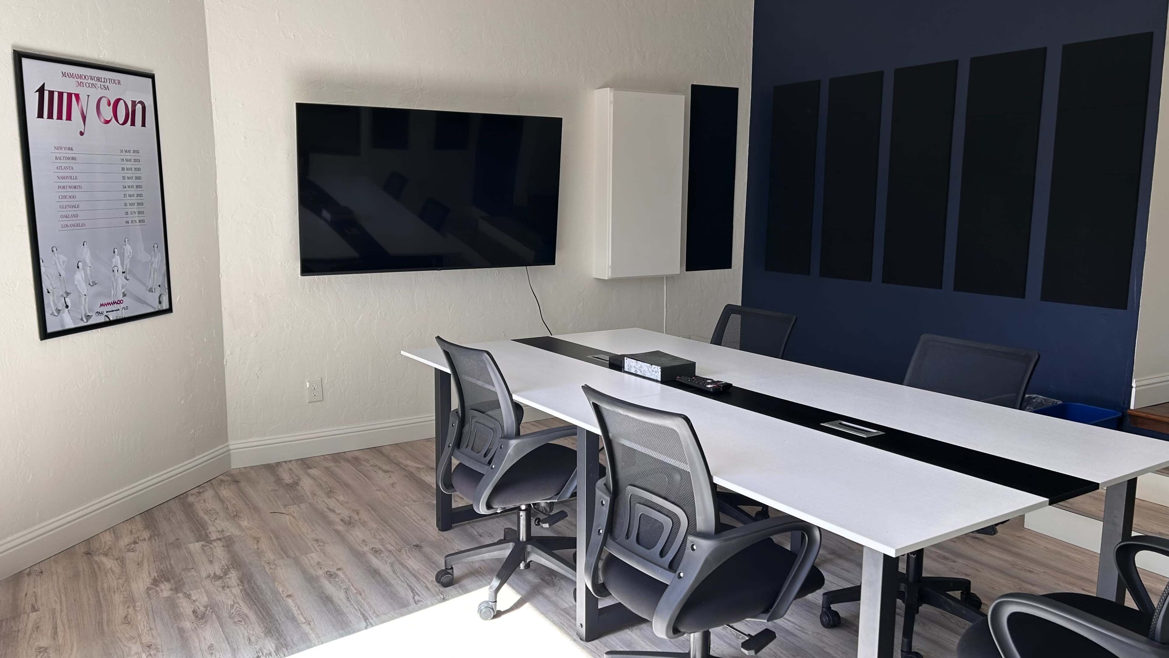 A modern conference room features a long table surrounded by ergonomic chairs, a large television on the wall, and sound-absorbing panels.