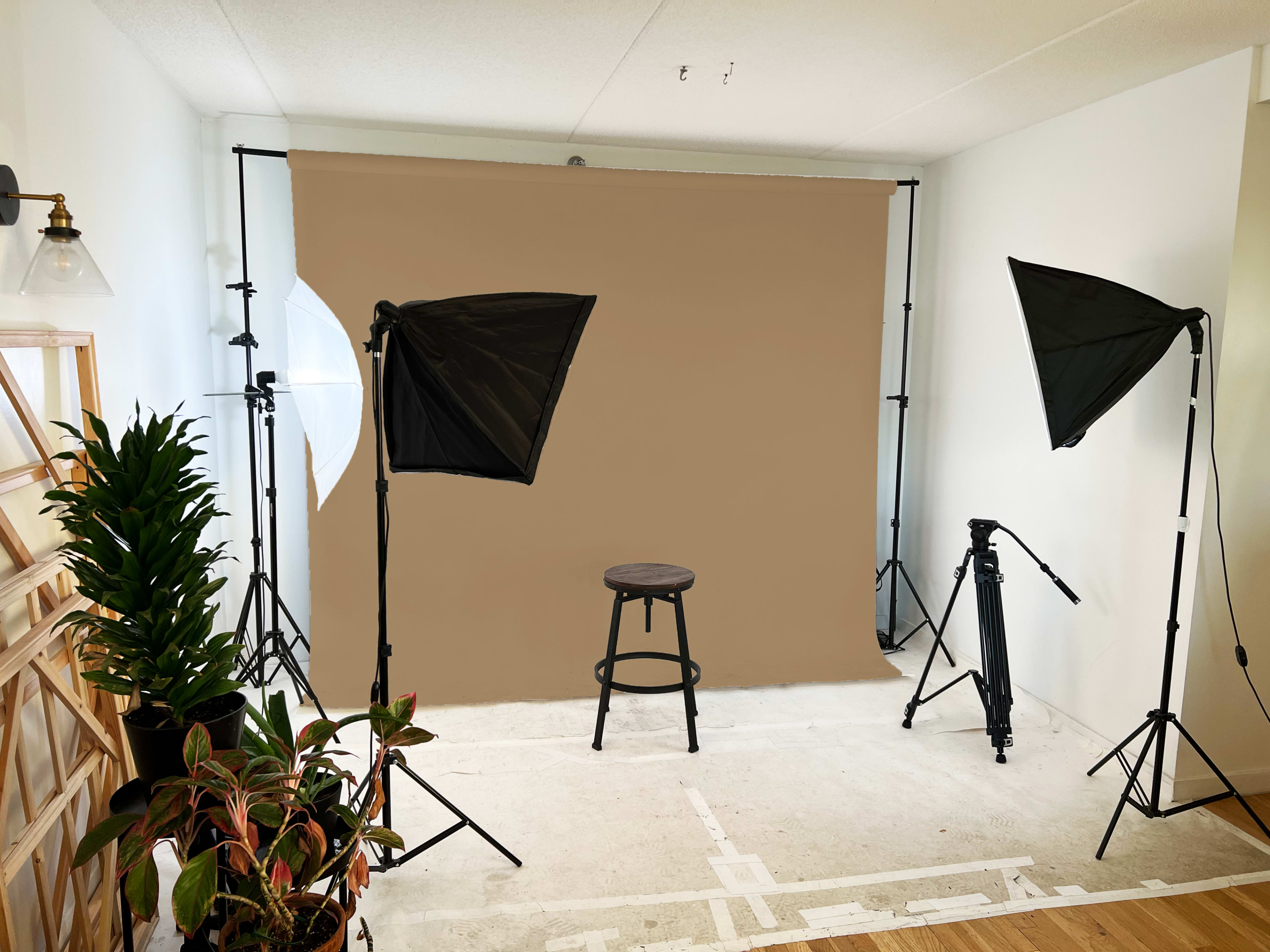 A photography setup featuring a beige backdrop, a wooden stool at the center, and two light panels on stands on either side.