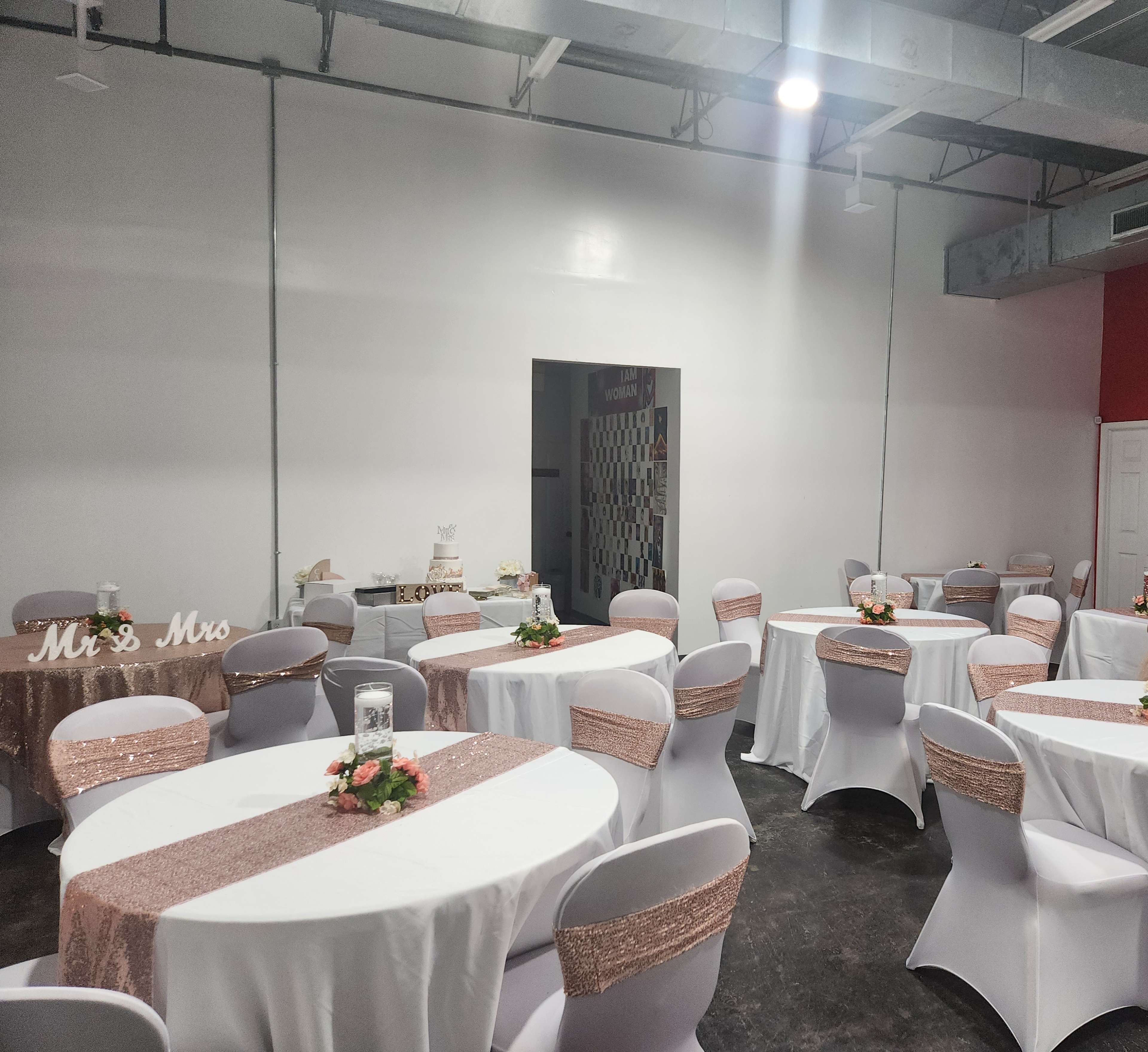 A banquet hall set up for a wedding reception, featuring round tables with white tablecloths and rose gold accents, along with a decorated dessert table in the background.
