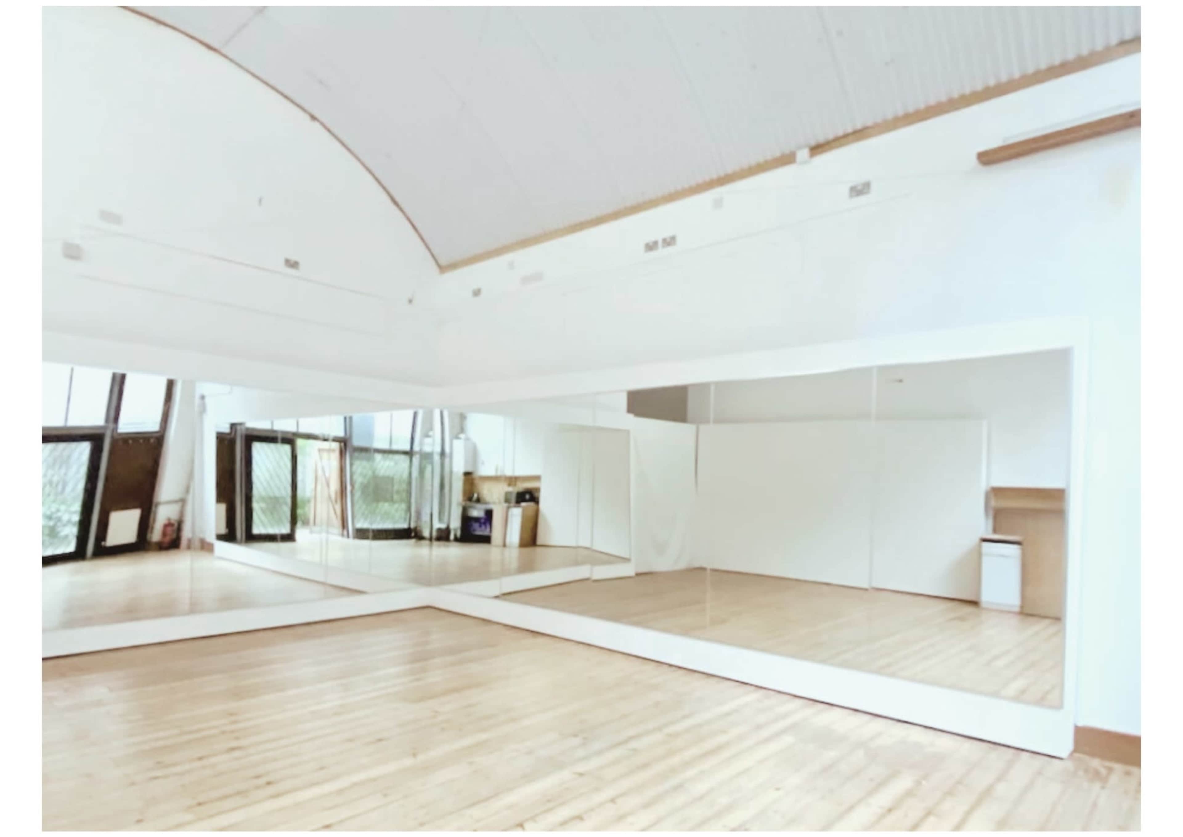 A spacious room with wooden flooring and large mirrors along one wall, reflecting the bright and open interior.