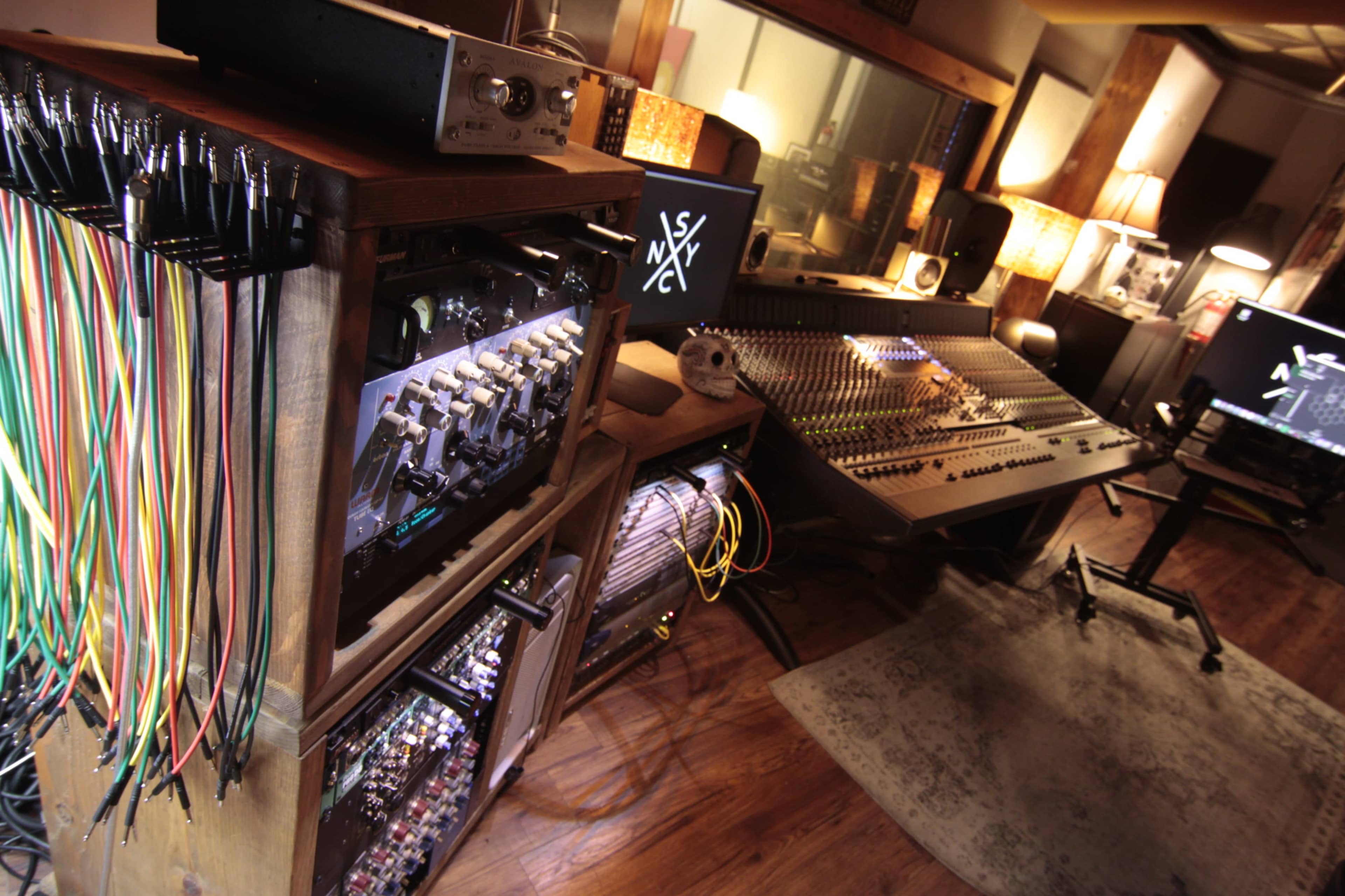 A music recording studio with a console, various cables, and electronic equipment arranged on wooden furniture.