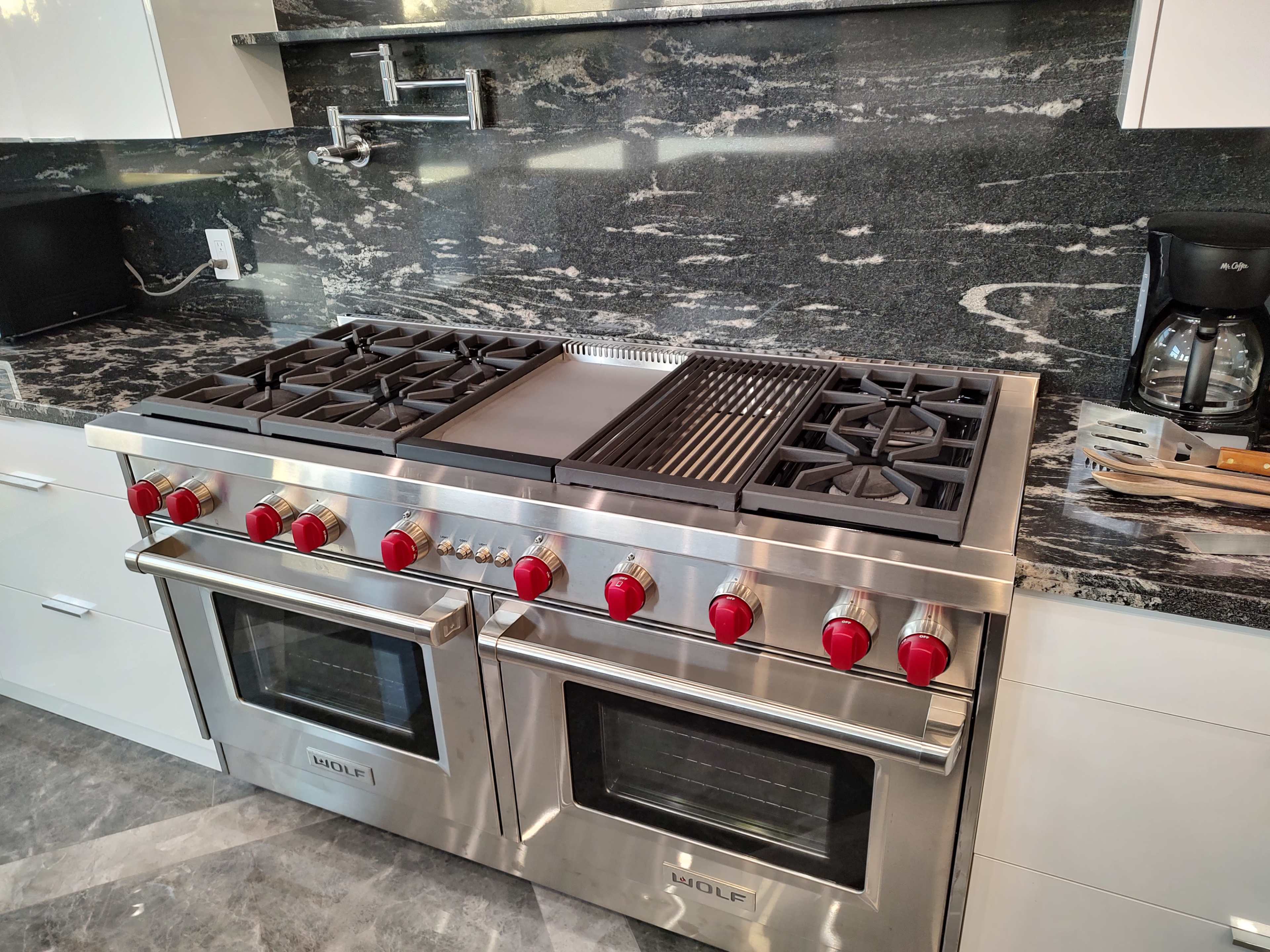 A stainless steel kitchen range with multiple burners, a griddle, and two ovens, set against a granite countertop and backsplash.