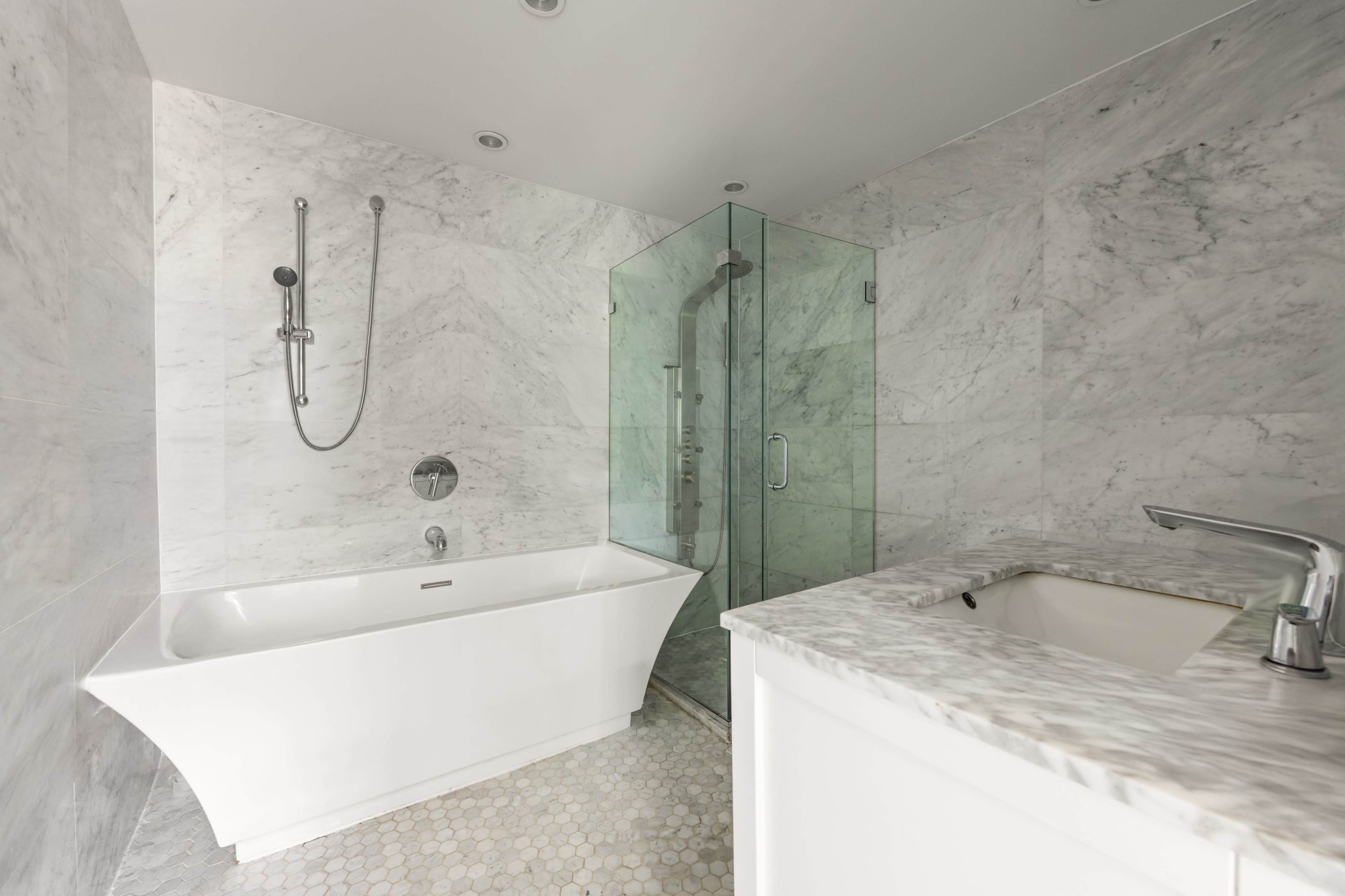 The bathroom features a white freestanding tub, a glass shower enclosure, and marble walls with a mosaic tile floor.