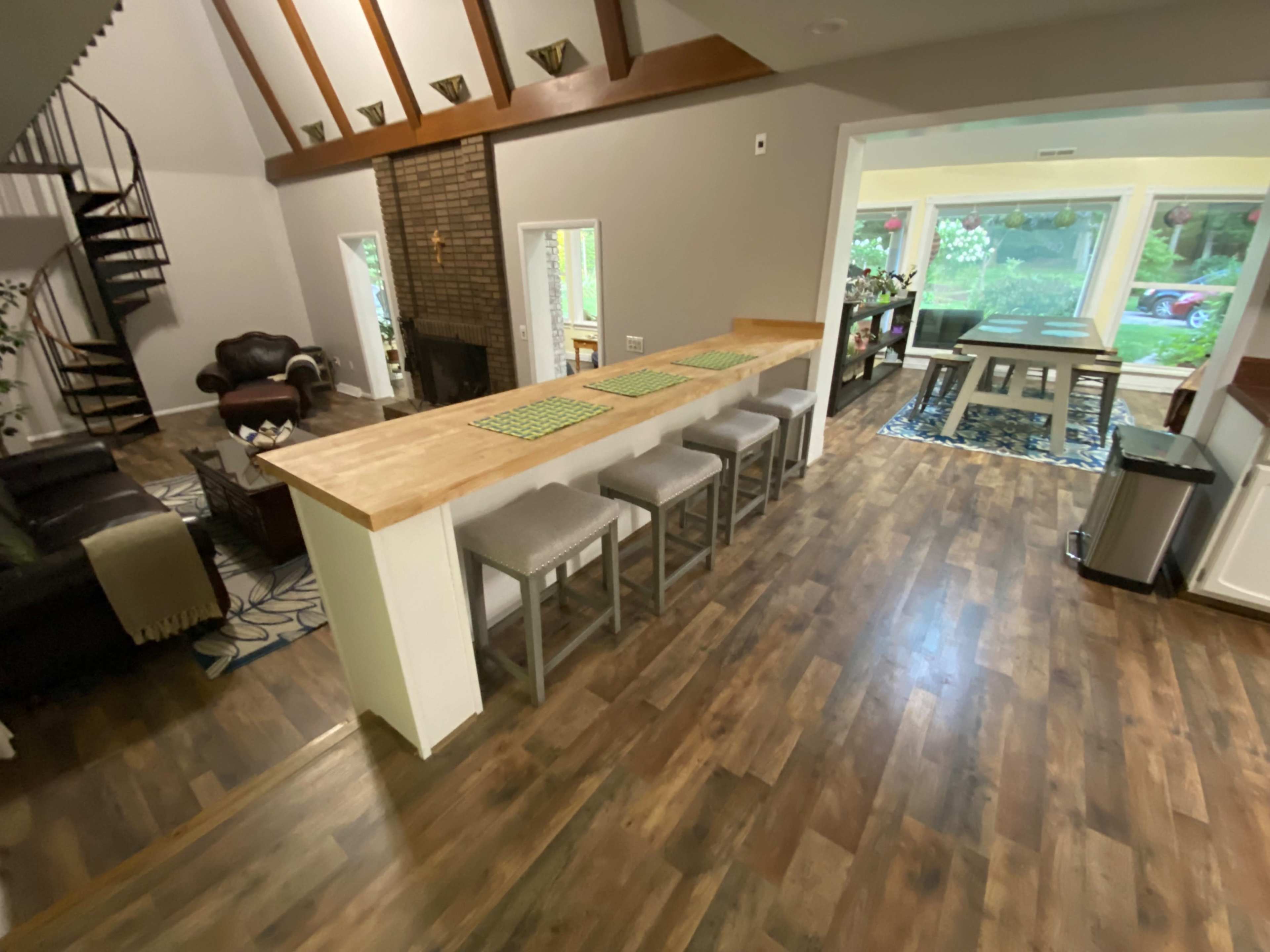 A spacious living area with a large wooden counter, seating for eight, and a view of a dining area through large windows.