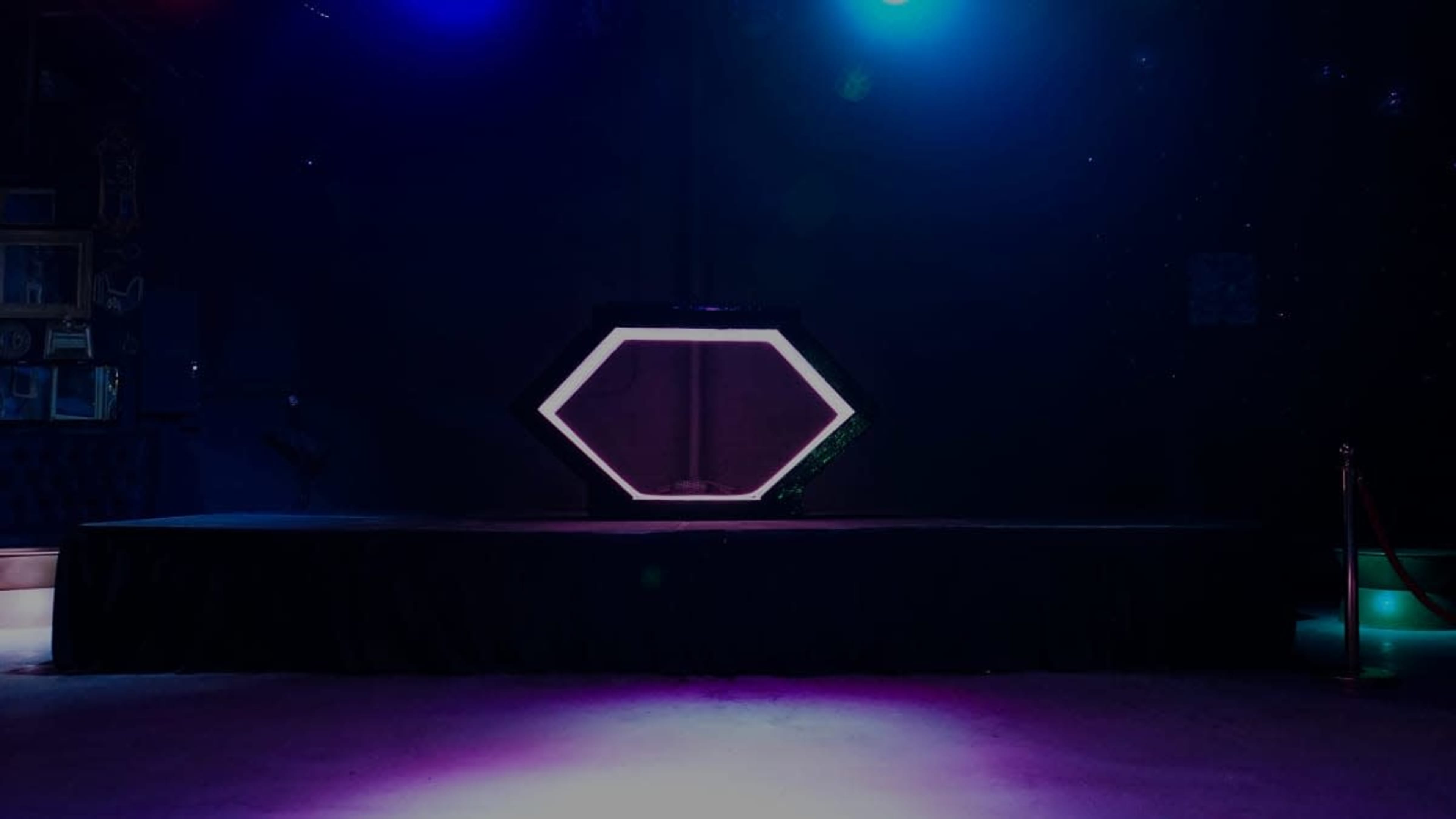 A hexagonal display stand is spotlighted on a dimly lit stage with colorful lighting effects.