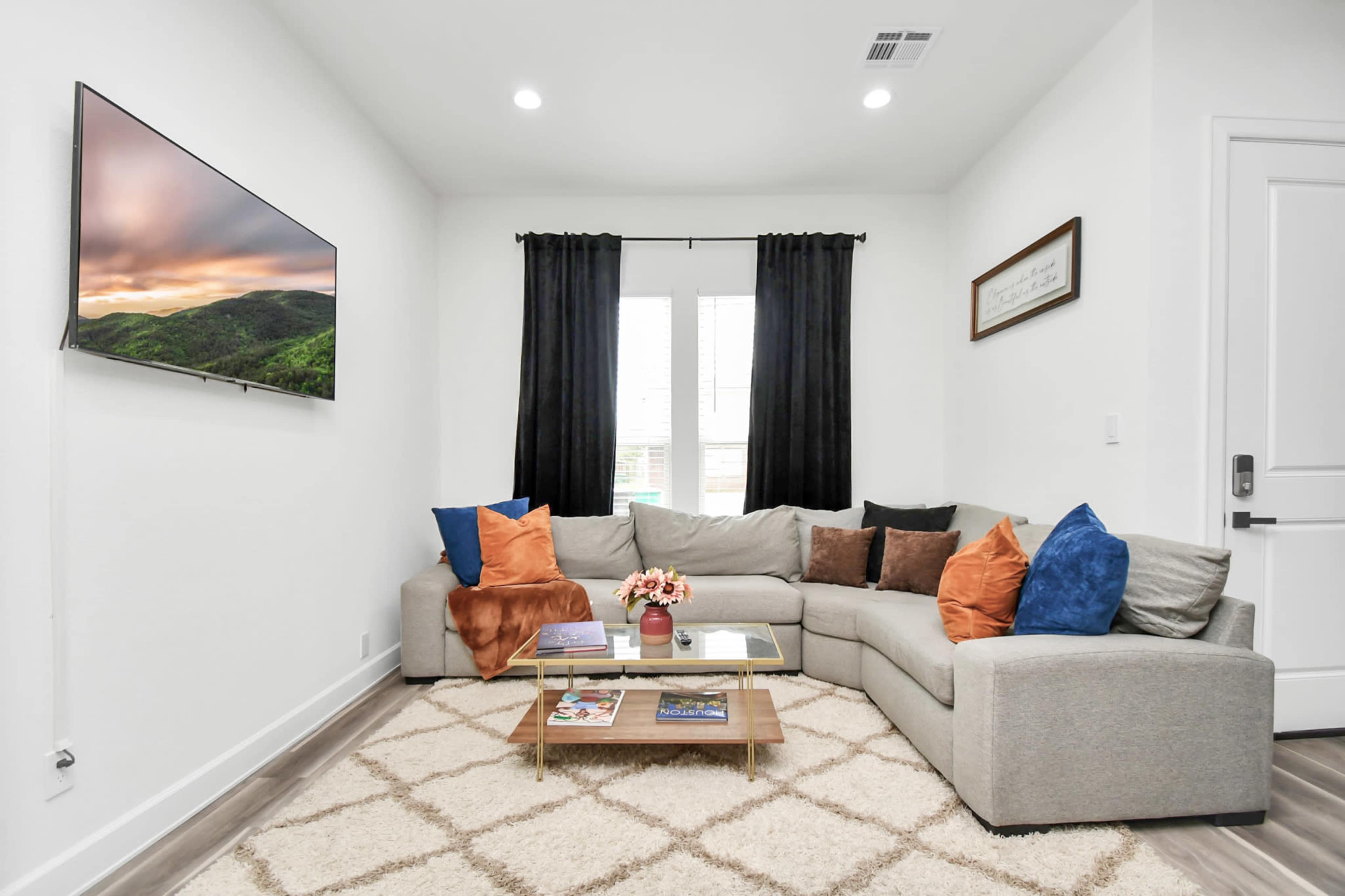 The living room features a sectional sofa with colorful pillows, a decorative coffee table, and a wall-mounted television.