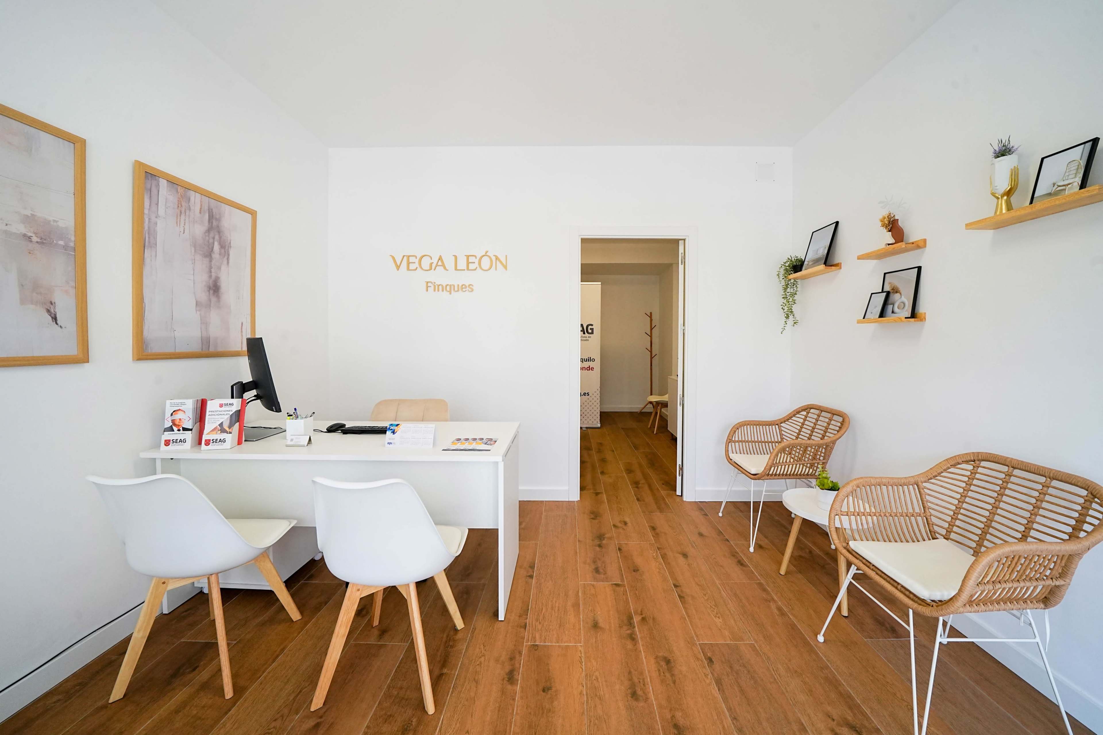 The image shows a modern, minimalist office space with a reception area, two white chairs, a desk, and decorative wall shelves.