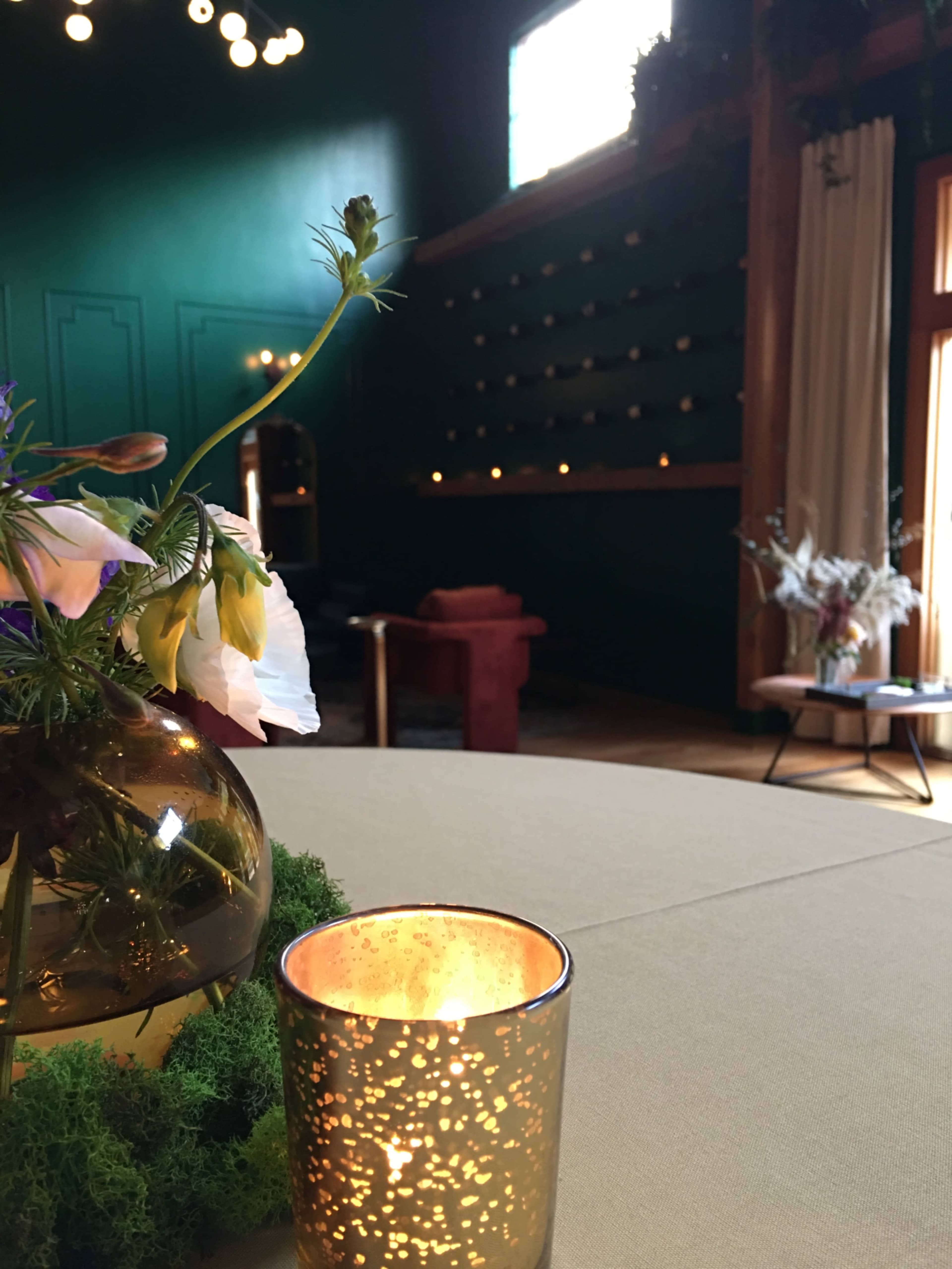 A dimly lit room with a green wall, featuring a wooden seating area and a table with a candle and flowers in a glass vase.