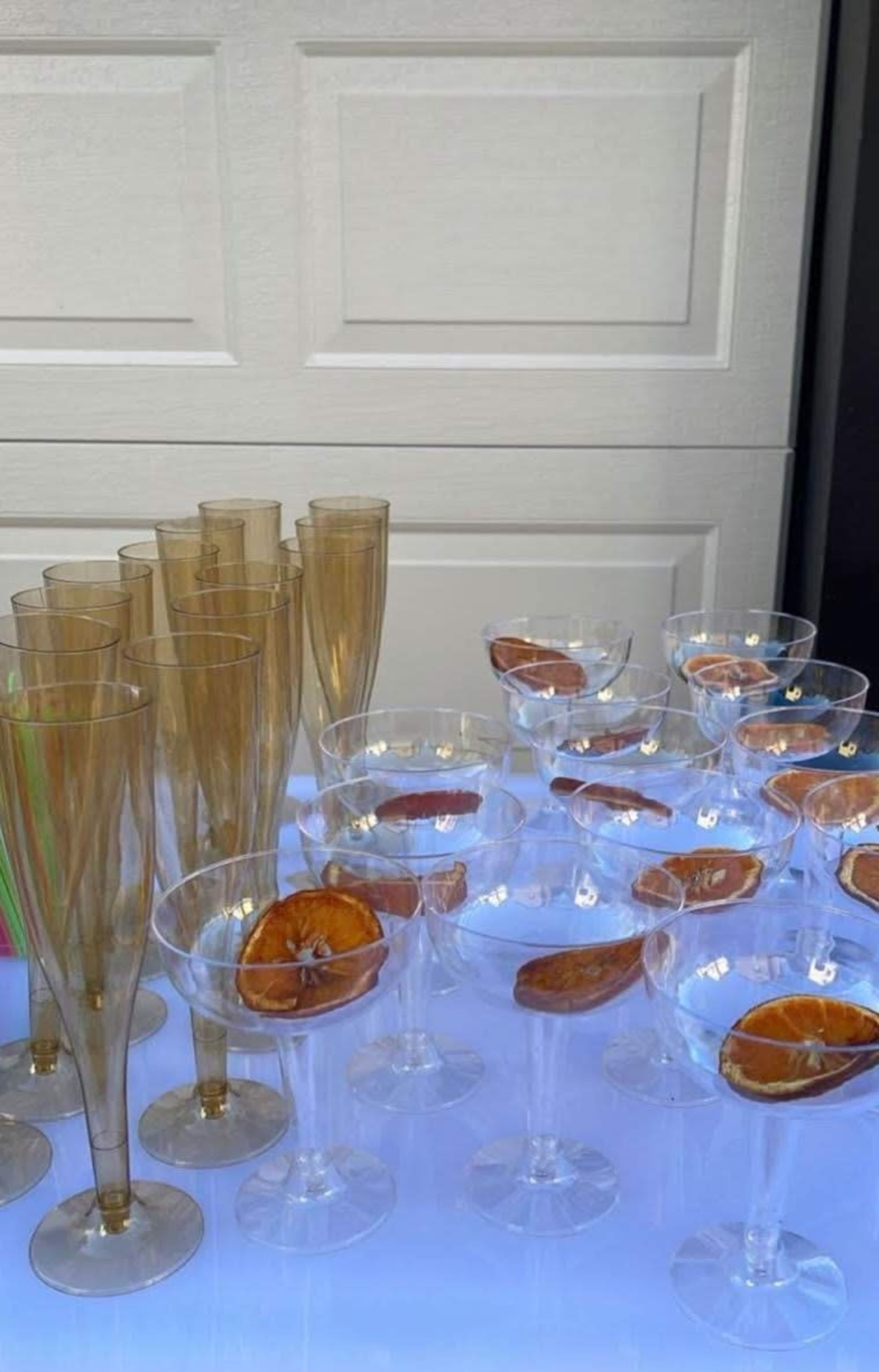 The image shows an assortment of clear and golden champagne glasses arranged on a table, each garnished with a slice of dried orange.