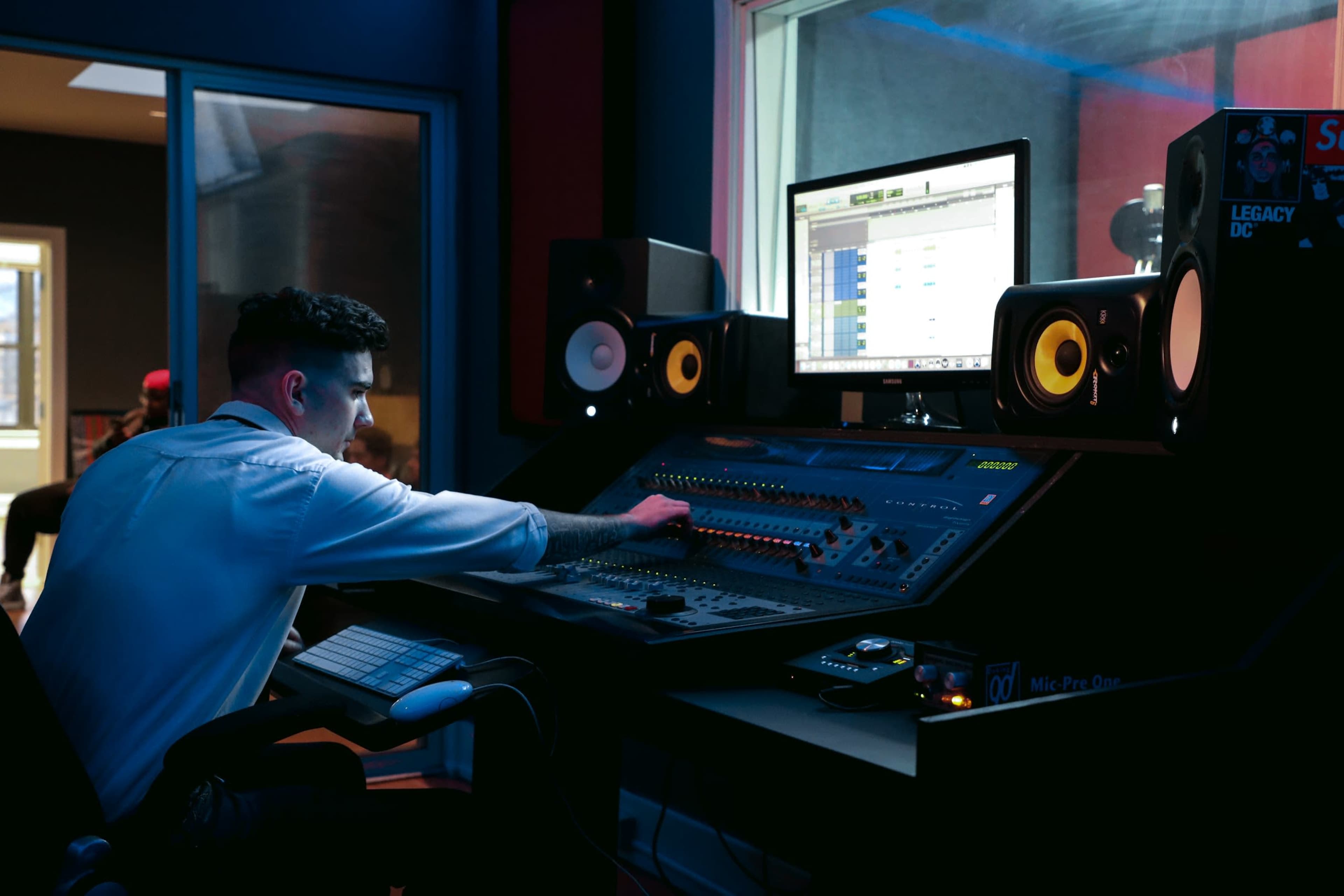 A sound engineer adjusts controls on a mixing console in a recording studio.