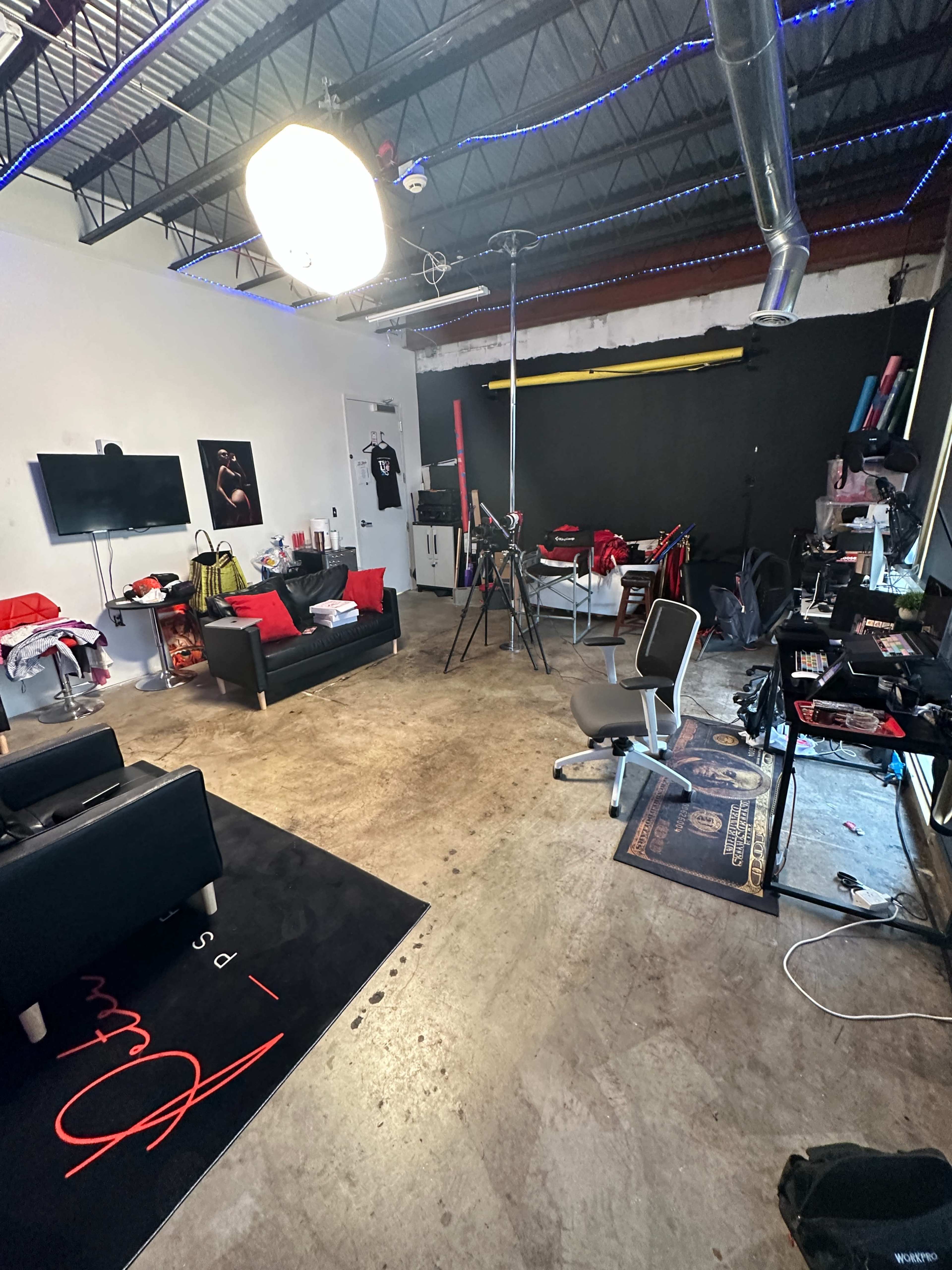 A cluttered studio space with a black wall, a couch, a television, and various equipment scattered throughout.