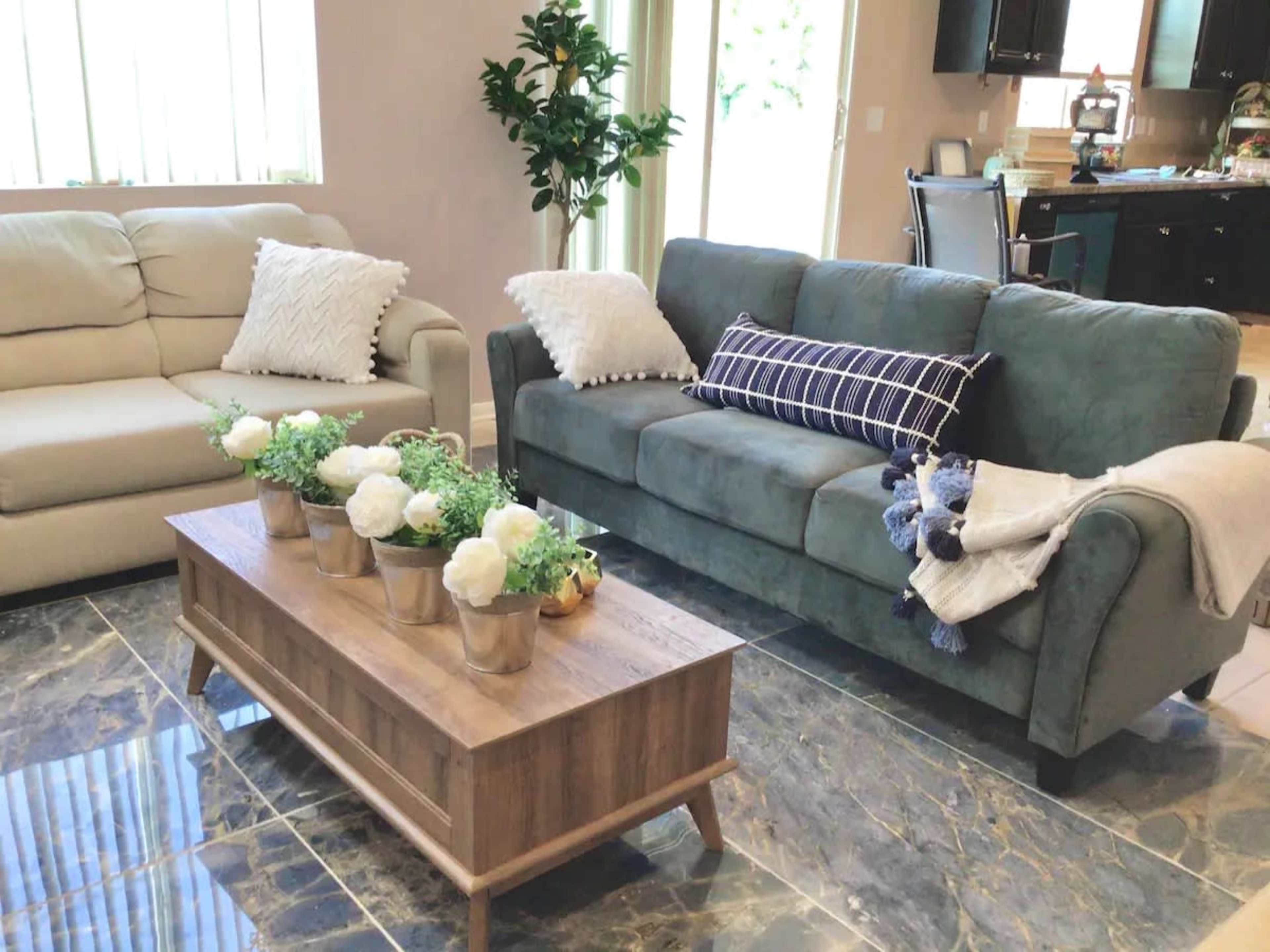 A living room with a green sofa, a beige couch, and a wooden coffee table decorated with potted plants and flowers.