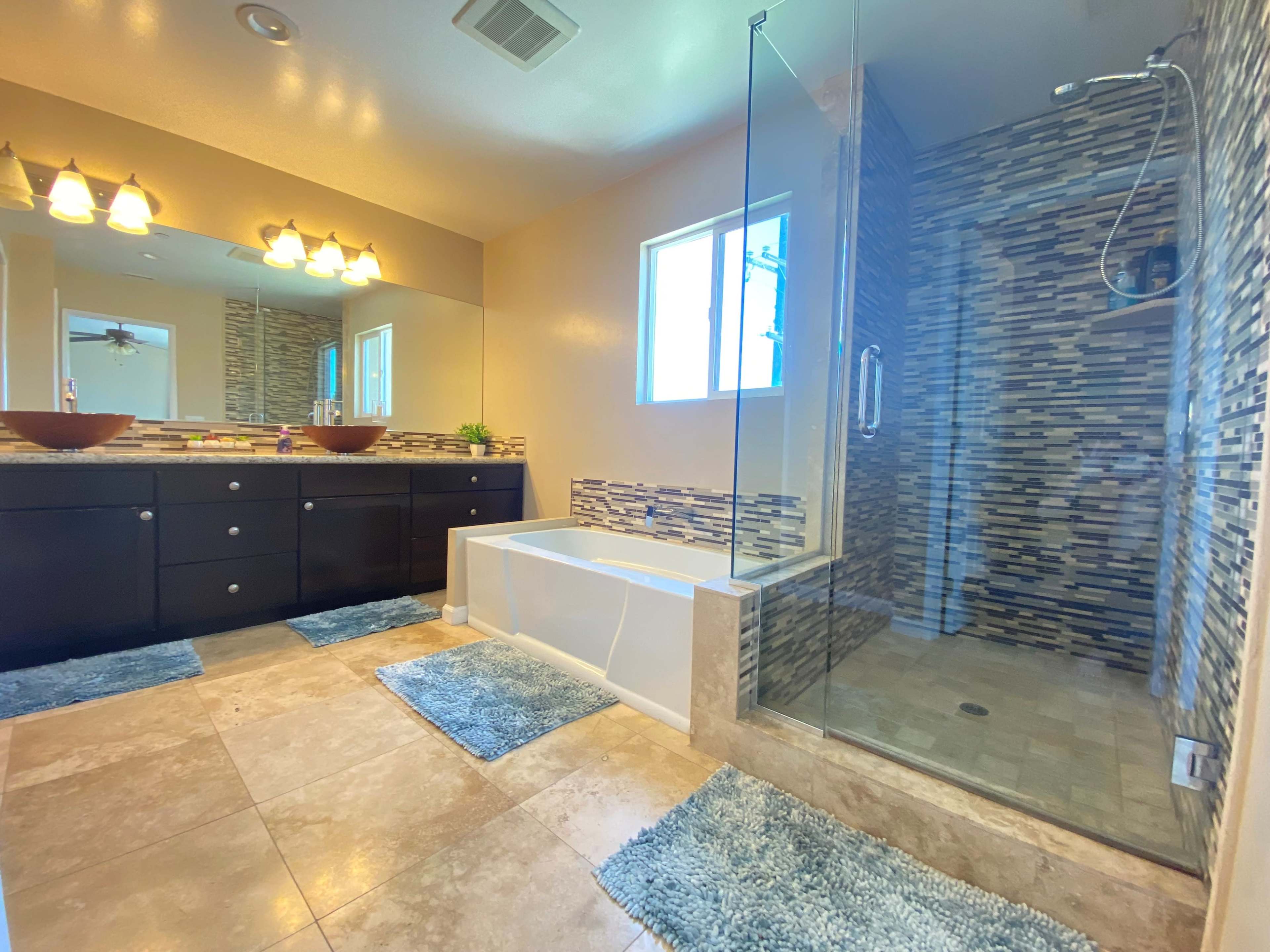 A modern bathroom featuring a double vanity with brown bowls, a separate shower with tiled walls, and a freestanding bathtub.