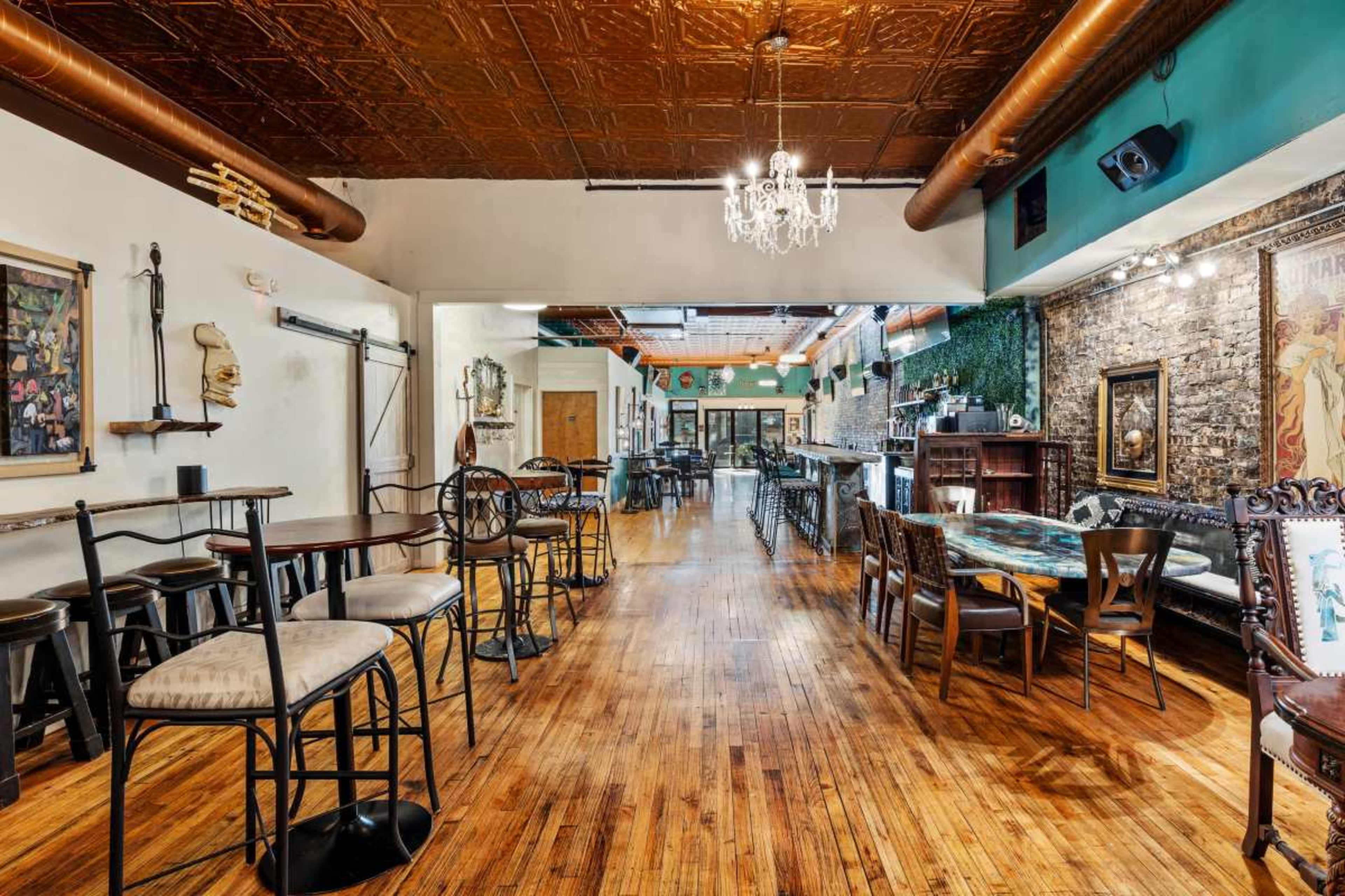 The image shows a spacious and well-lit restaurant or bar interior featuring wooden floors, brick walls, and a mix of high and low seating arrangements.