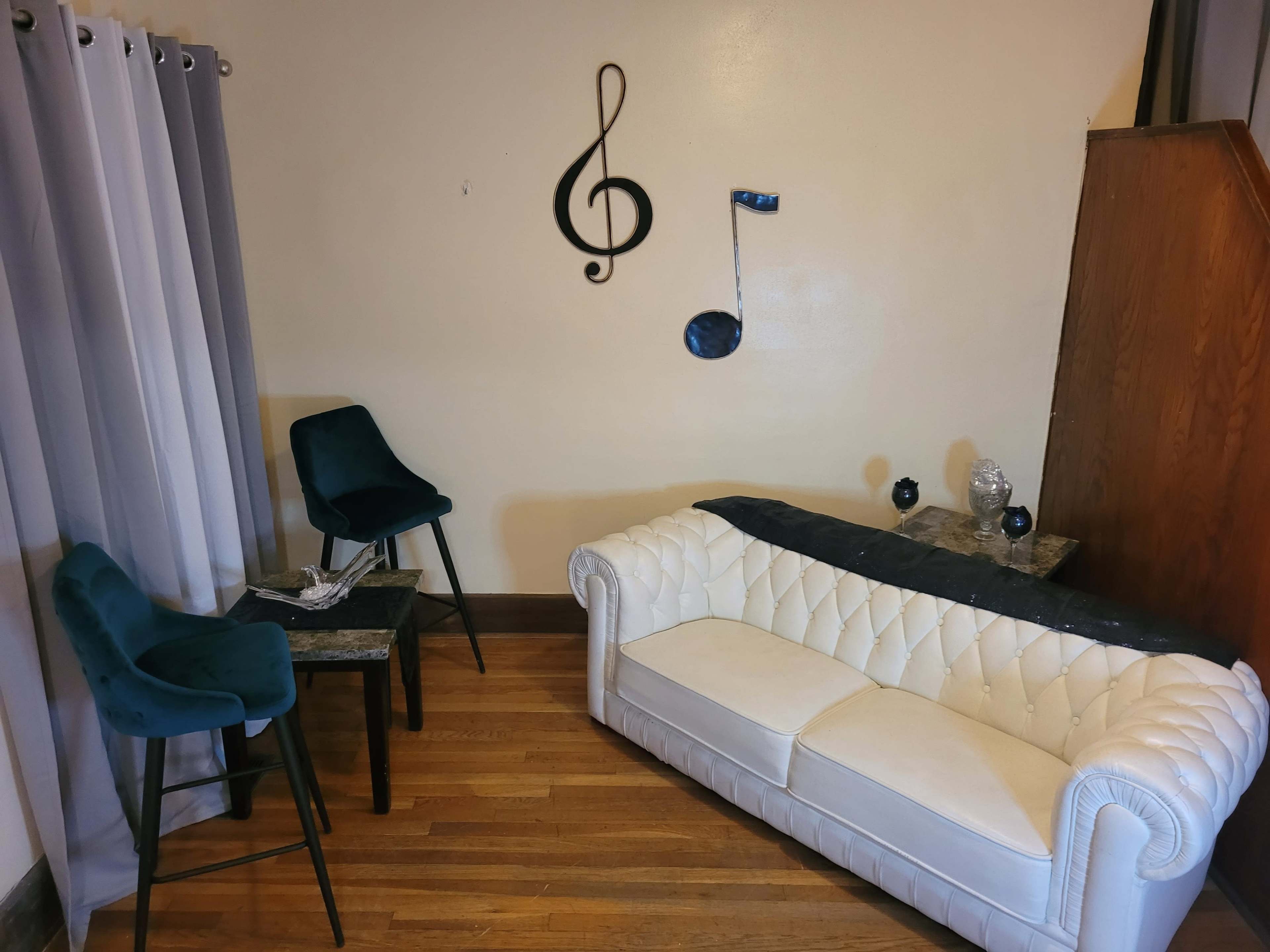 The room features a white tufted sofa, a small table with two dark chairs, and musical note decorations on the wall.