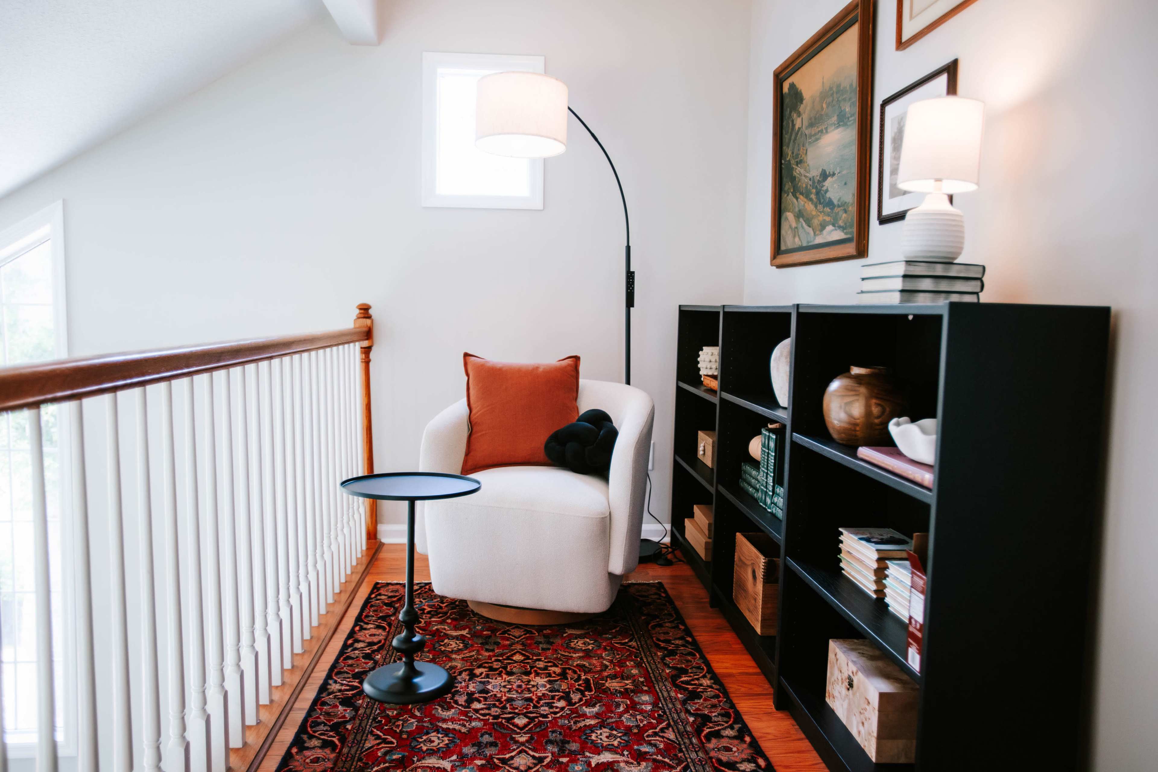 The image shows a cozy nook with a white armchair, a small side table, and a bookshelf filled with decorative items, all set against a backdrop of light-colored walls and wood flooring.