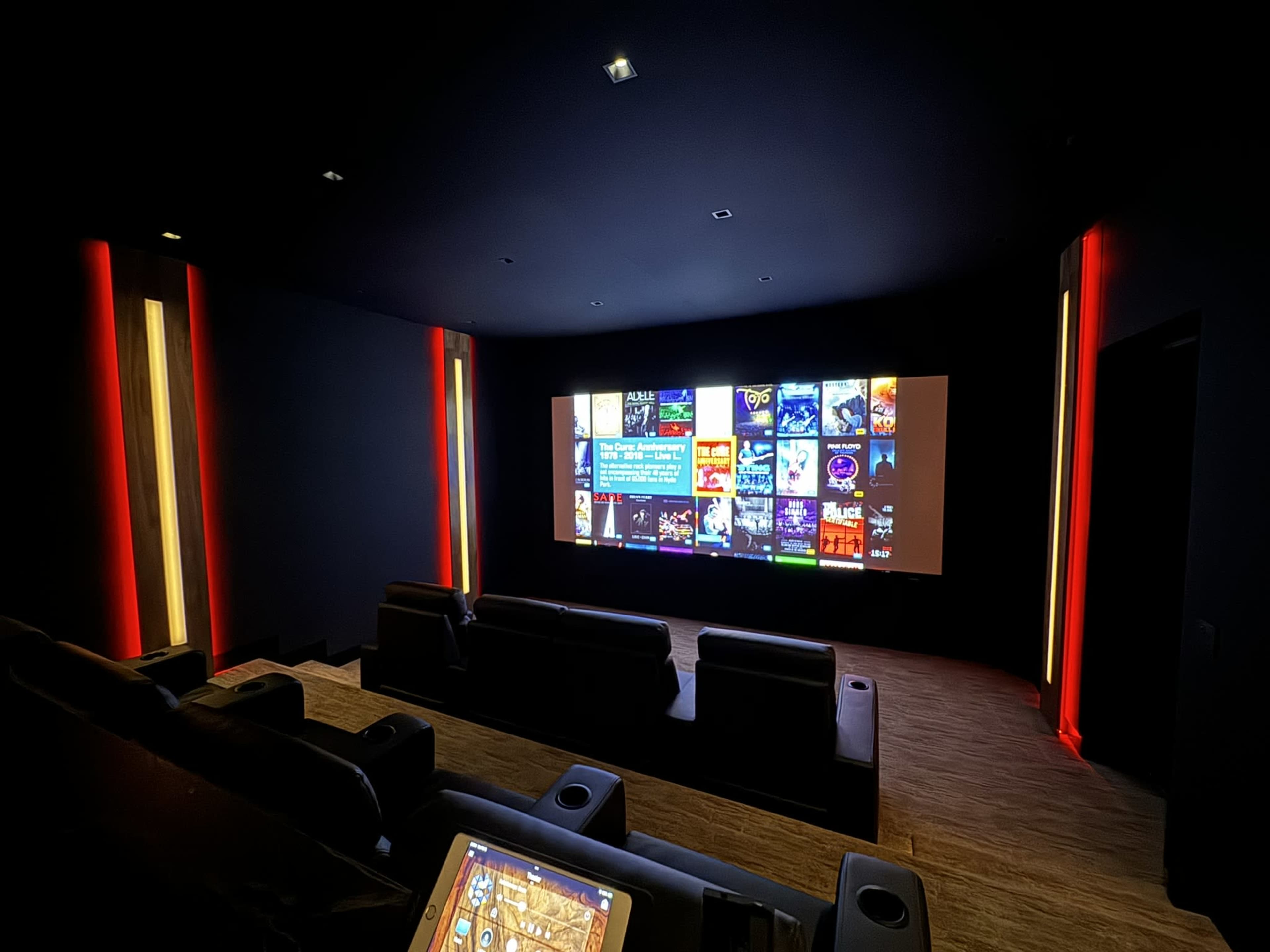 A darkened home theater with black leather seating and a large screen displaying various movie and show options.