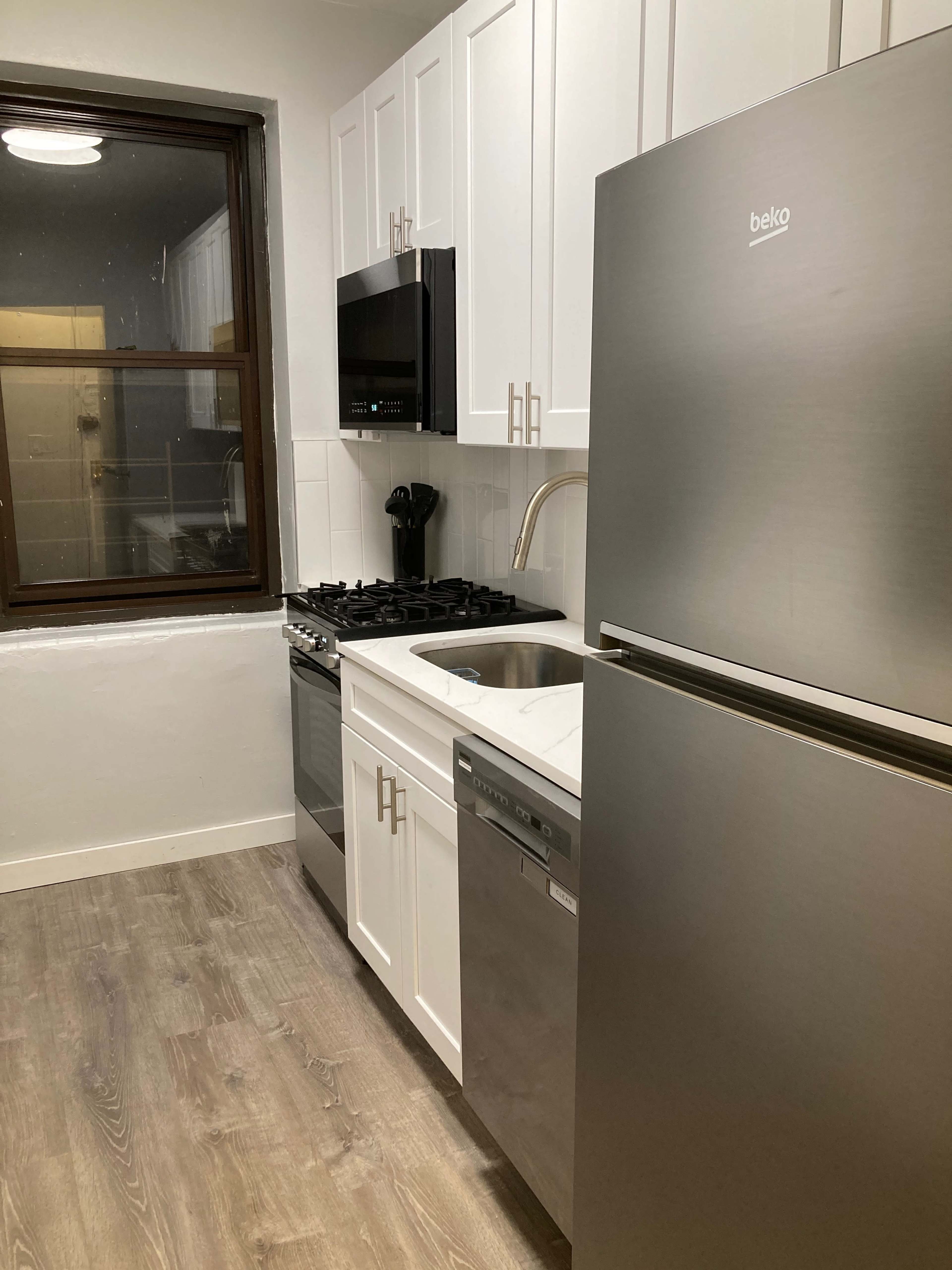 A modern kitchen featuring white cabinetry, a stainless steel refrigerator, a gas stove, and a dishwasher along with a window above the sink.